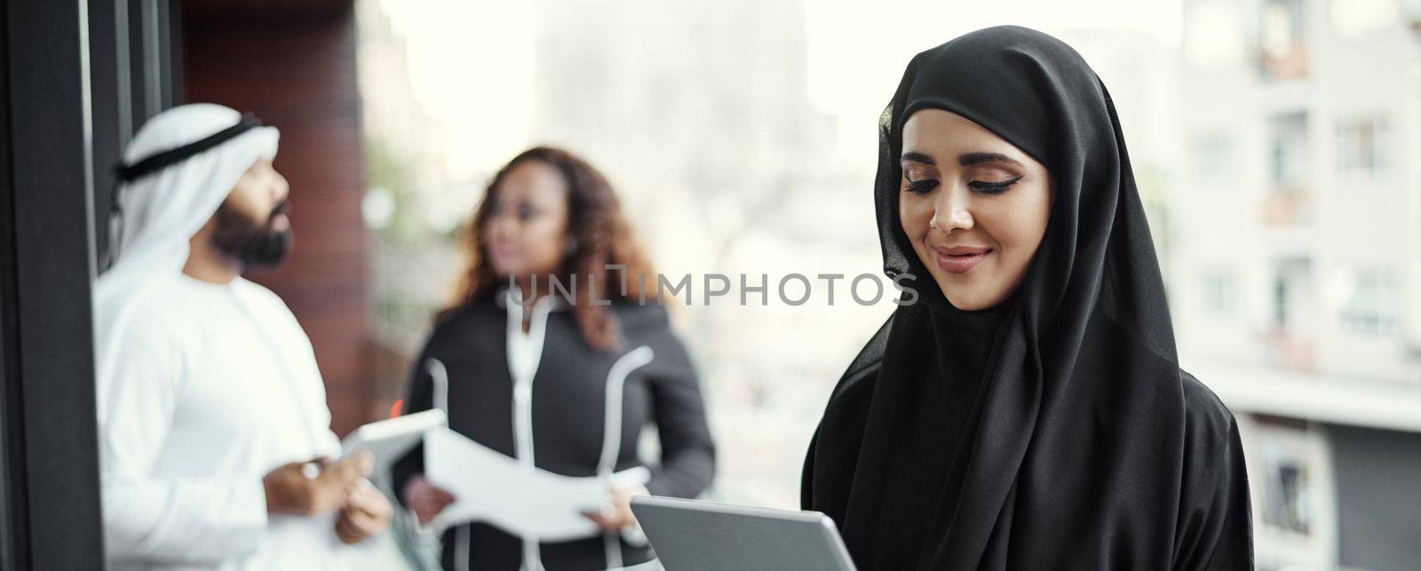 Shes happy with her progress. an attractive young businesswoman dressed in Islamic traditional clothing using a tablet on her office balcony