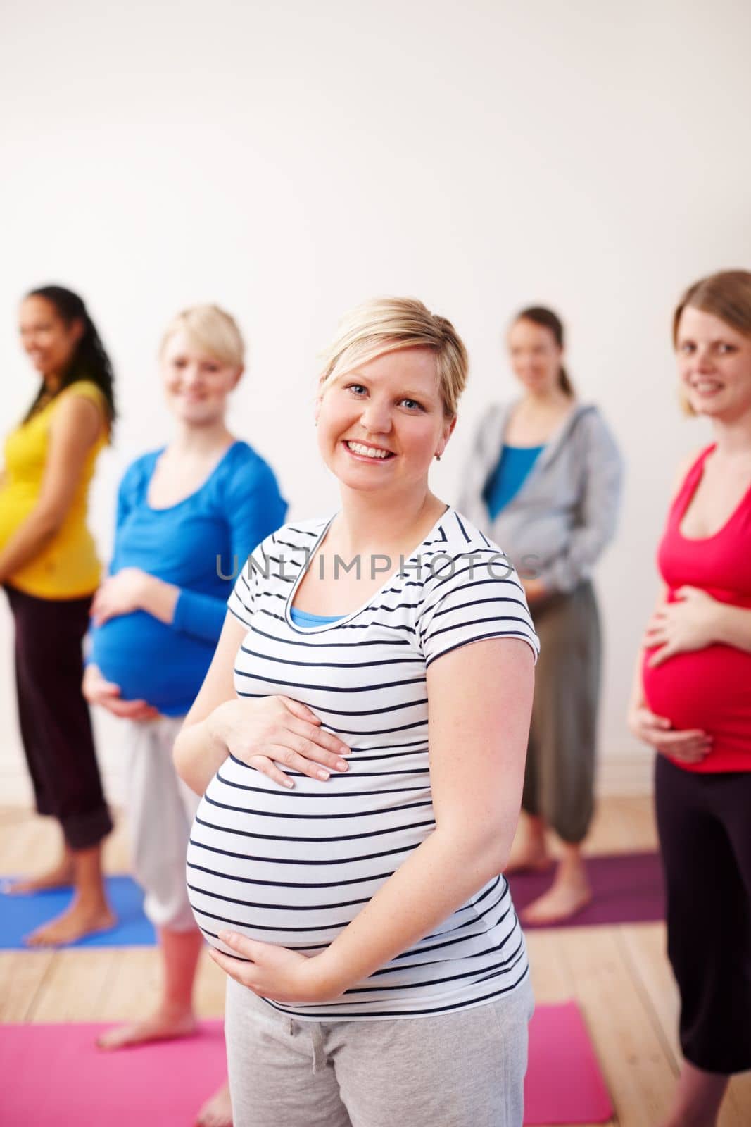 Making the most of maternity. A multi-ethnic group of pregnant women standing in an exercise class smiling happily at the camera. by YuriArcurs