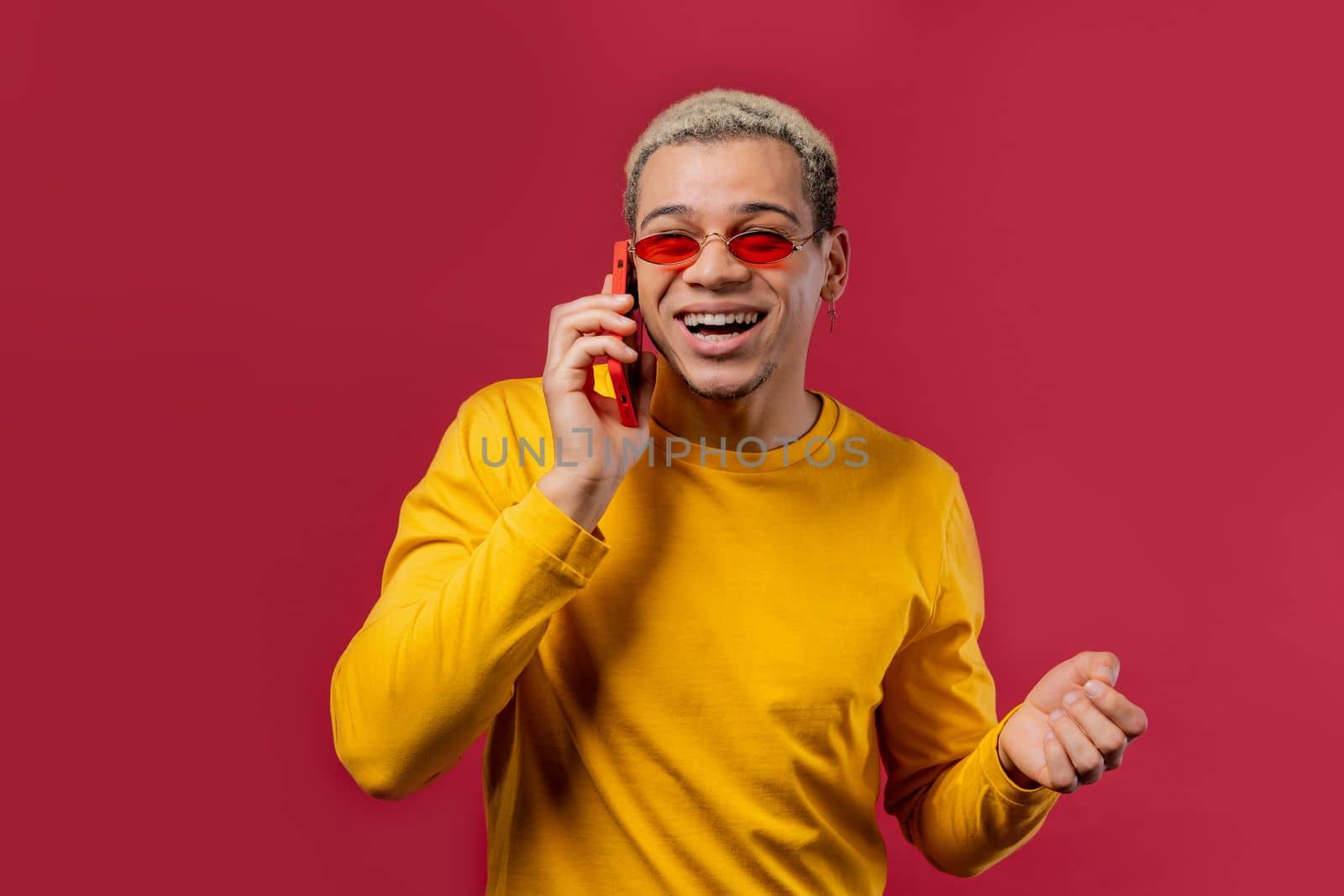 Stylish man talking by phone, nice joke, smiling. Young guy on red background. Having smartphone call. . High quality photo