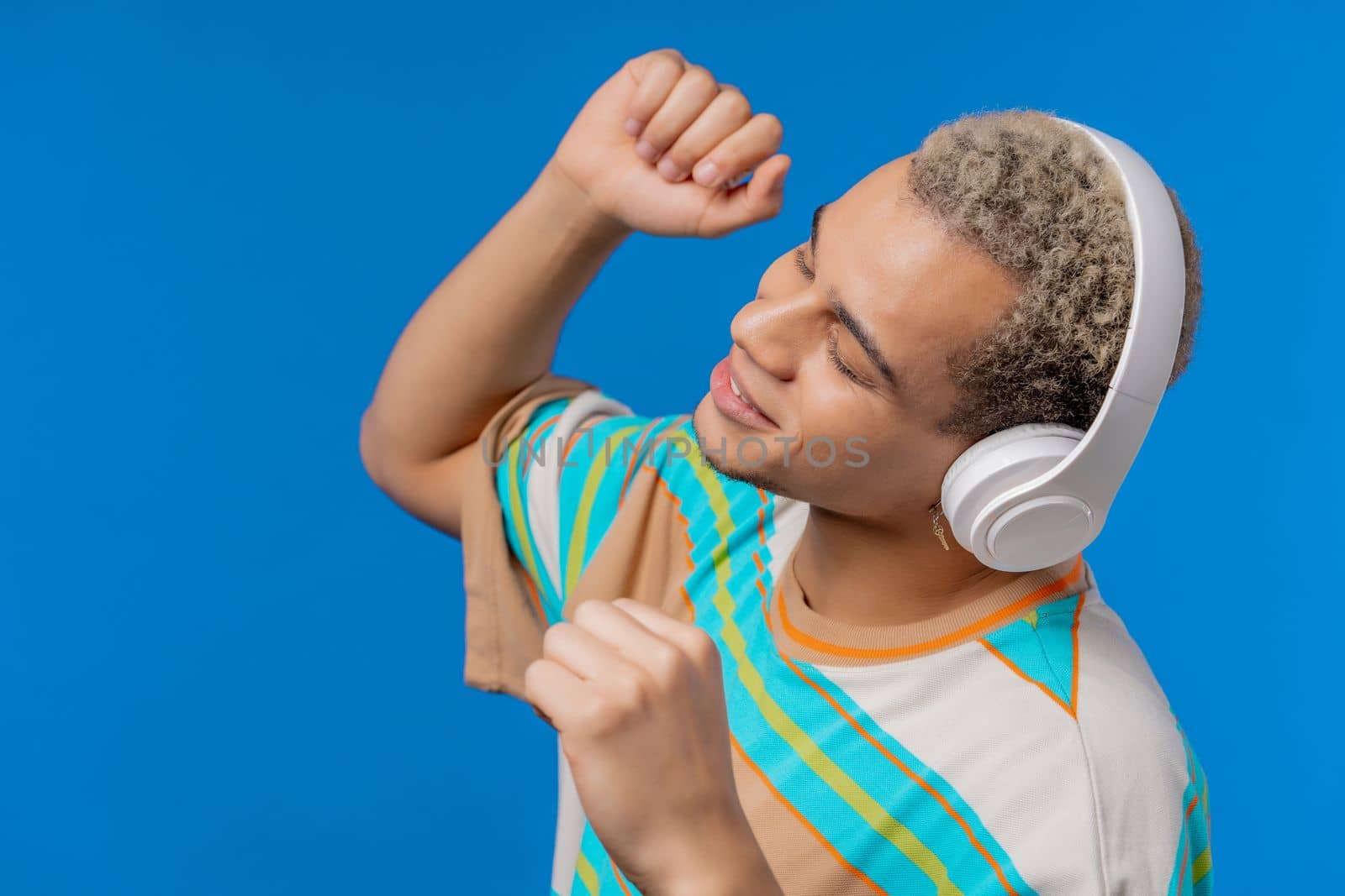 Positive man listening music, enjoying dance with headphones on blue studio background. Radio, wireless modern sound technology, online player. High quality photo