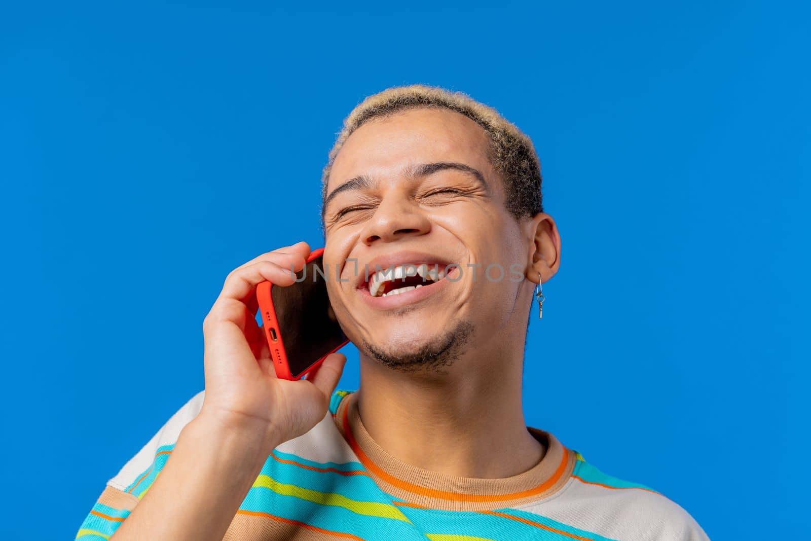 Smiling positive man talking by phone, nice joke, smiling. Young guy on blue background. Having smartphone call. . High quality photo