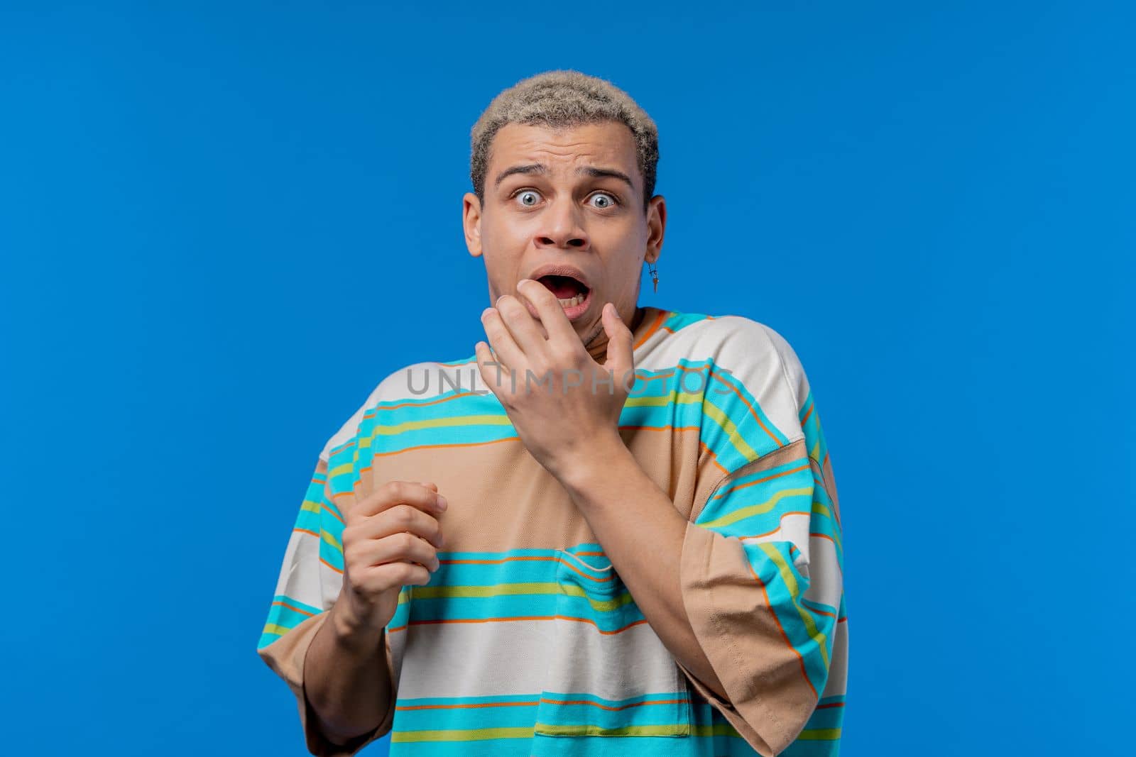 Frightened shocked man afraid of something and looks into camera with big eyes full of horror on blue background. Phobia, trouble, panic concept. High quality photo