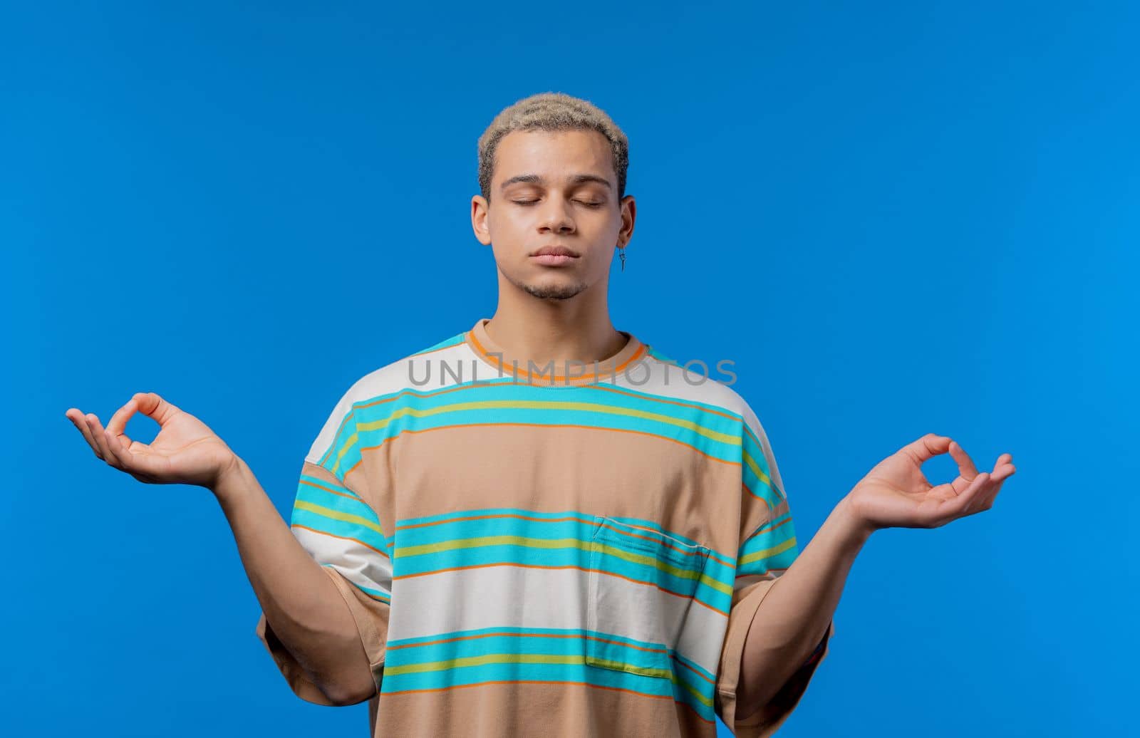 Calm man relaxing, meditating, refuses stress. Curly haired guy breathes deeply, calms down blue studio background. Yoga, moral balance, zen concept. High quality photo