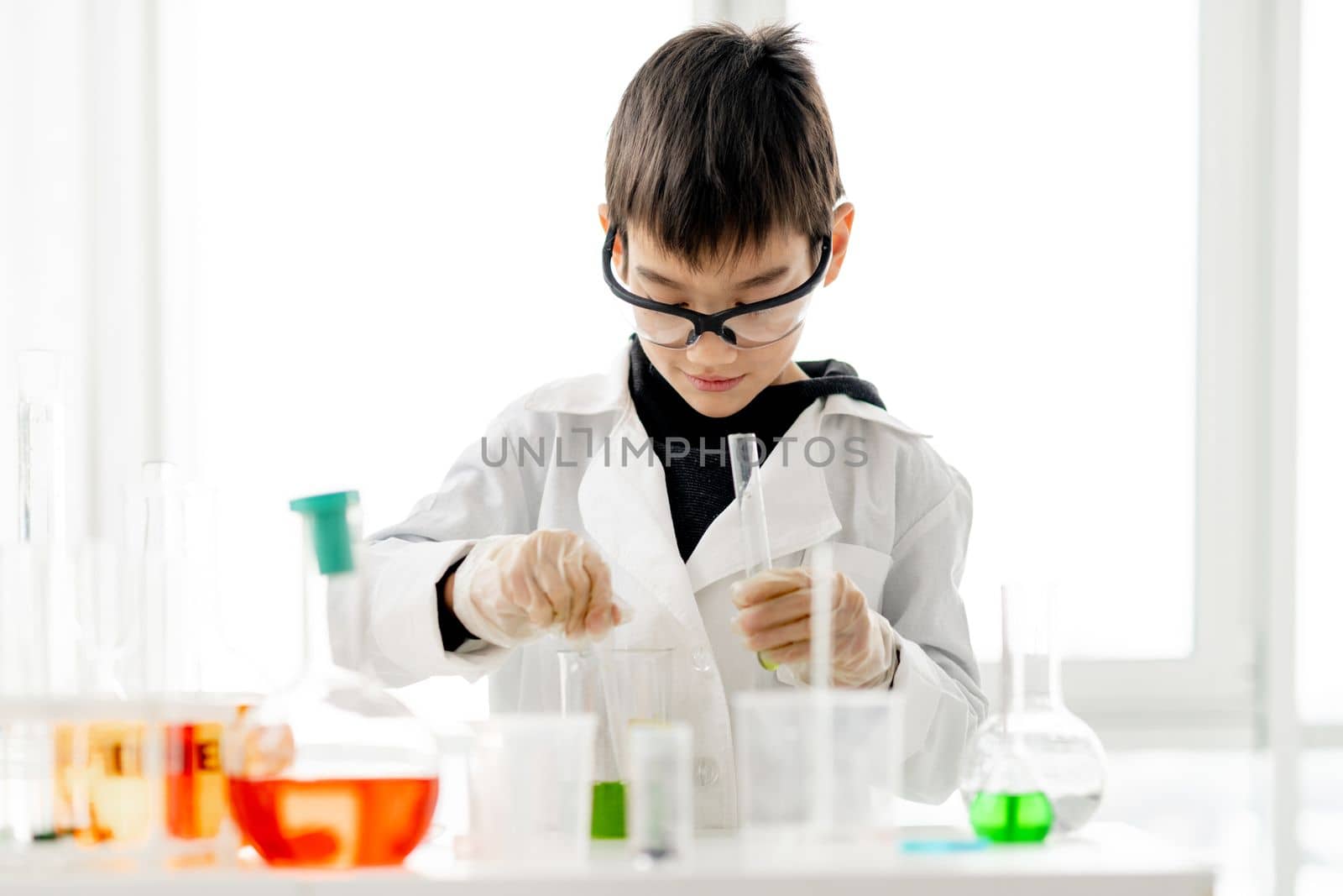 School boy wearing protection glasses doing chemistry experiment in elementary science class. Clever pupil with dander mark bottle in lab