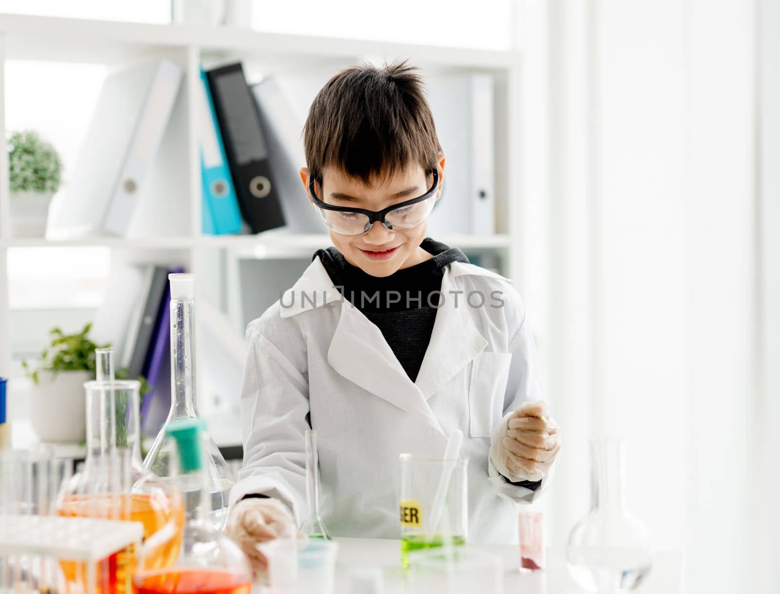 School boy wearing protection glasses doing chemistry experiment in elementary science class. Pupil with equipment tubes in lab