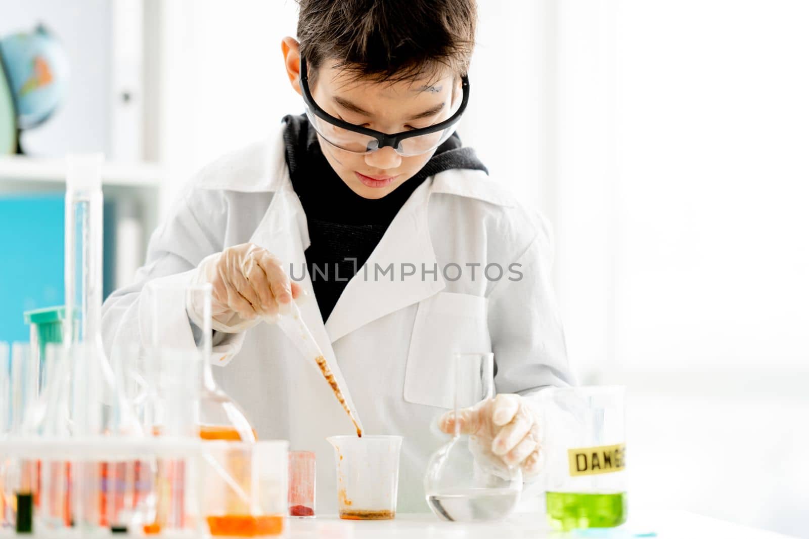 School boy wearing protection glasses with dirty face doing chemistry experiment with chemical liquids in elementary science class. Clever pupil analyzing results of test in lab