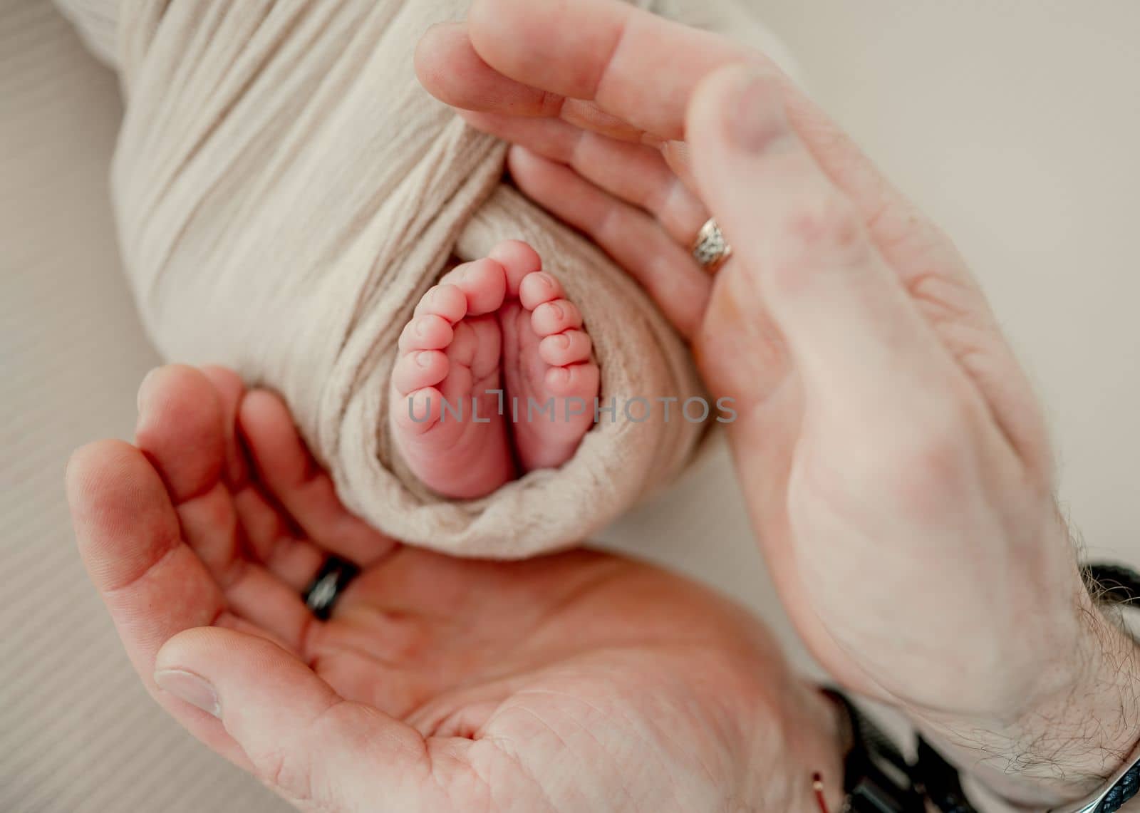 Father holding little baby's legs wearing in white knitted pants