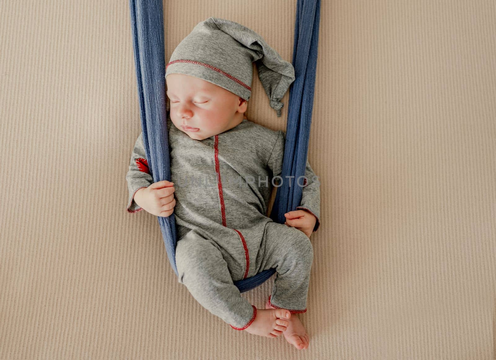 Newborn baby boy sleeping with knitted heart toy during studio photoshoot. Adorable infant child kid sleeping wearing hat and costume