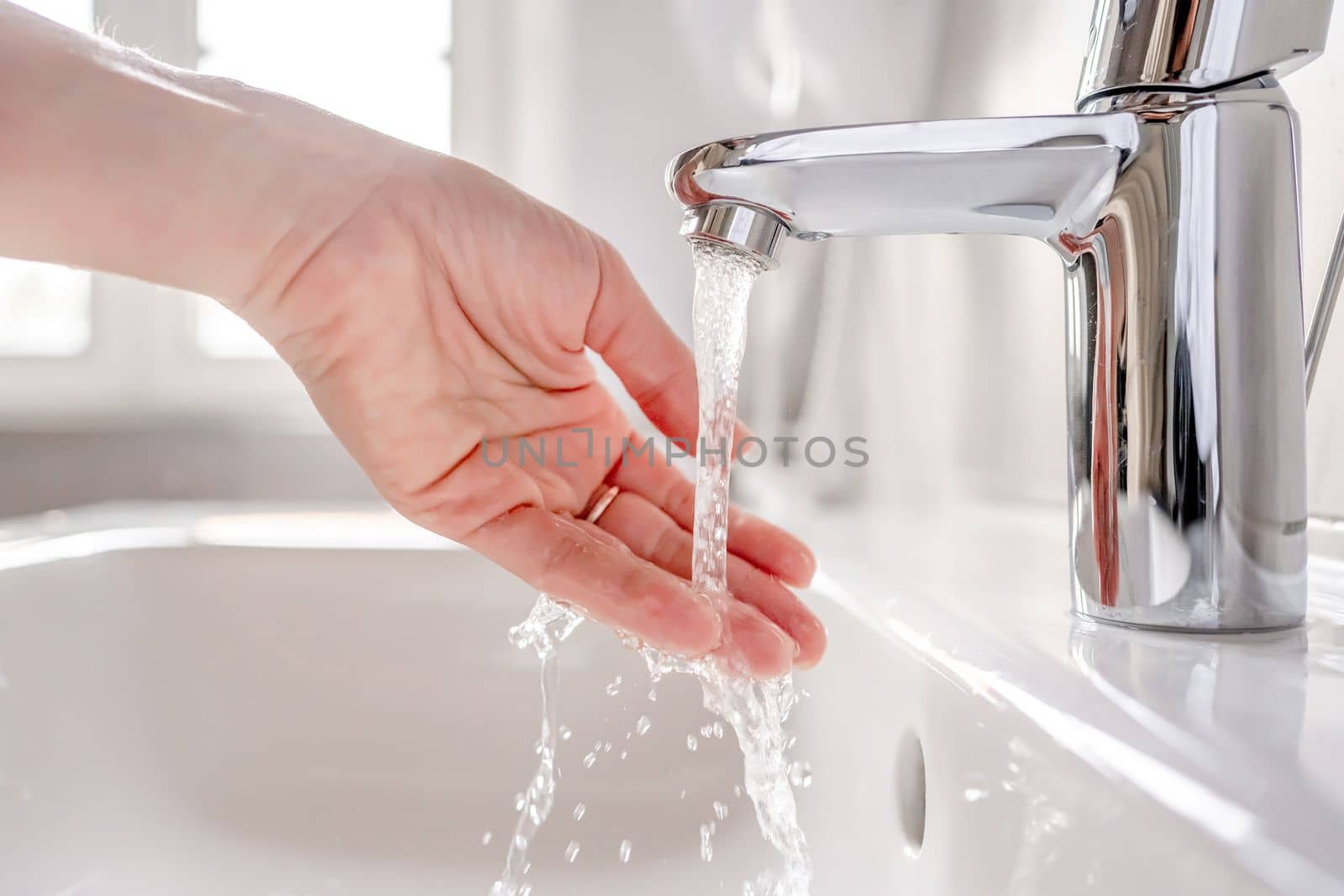 Young woman washes her hands with soap over the sink in the bathroom, close-up.