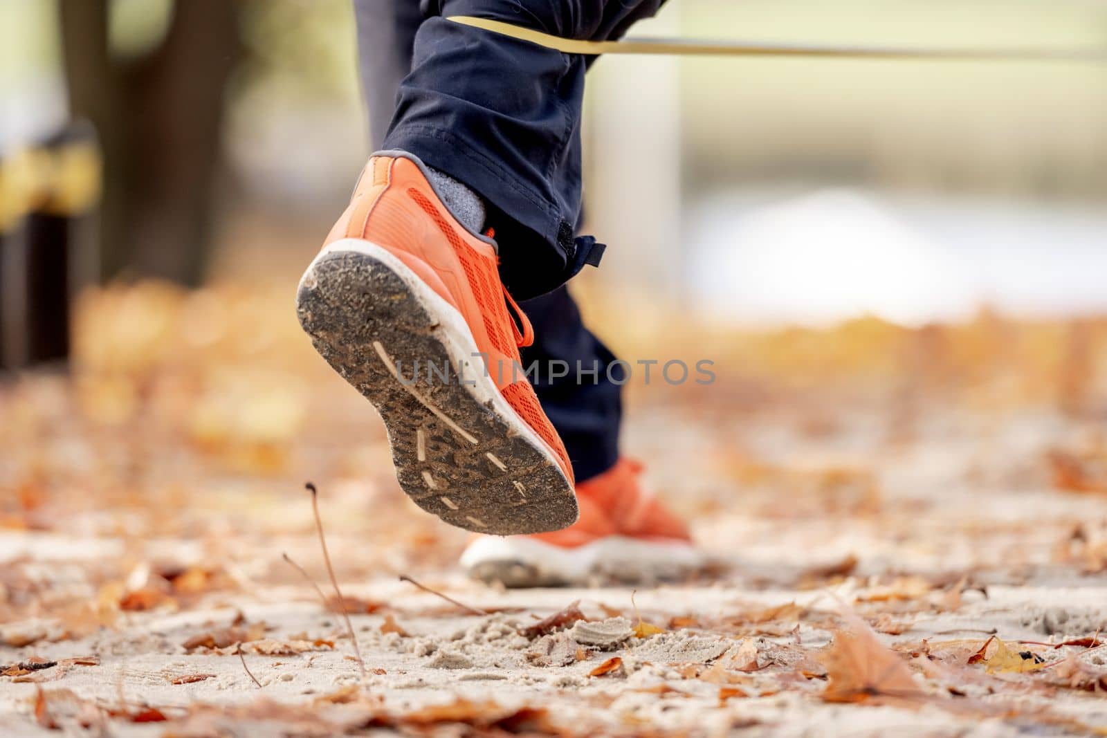 Strong man guy training with elastic rubber band at the autumn stadium outdoors. Adult male person during workout for legs with additional sport equipmant. Sportsman exercising outside
