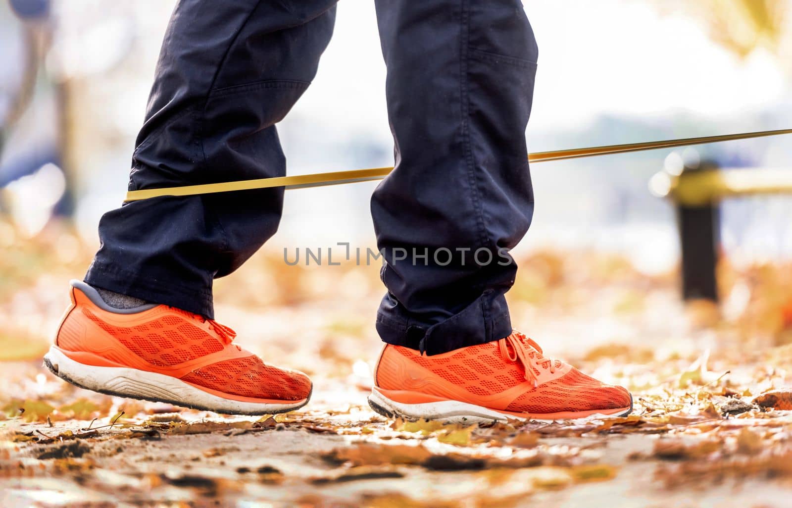 Strong man guy training with elastic rubber band at the autumn stadium outdoors. Adult male person during workout for legs with additional sport equipmant. Sportsman exercising outside