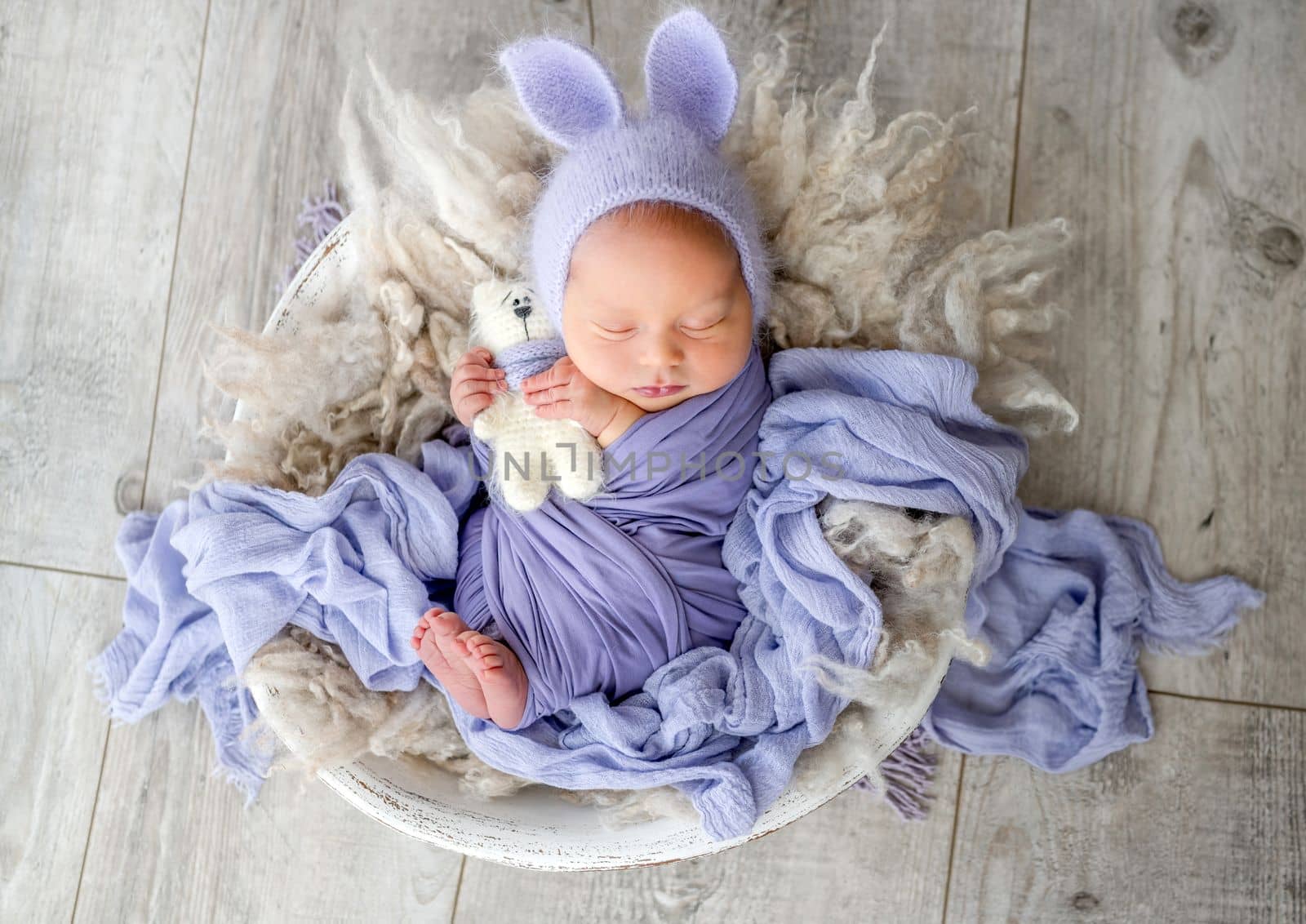 Newborn baby boy sleeping with kitty toy and smiling. Little infant child swaddled in fabric napping