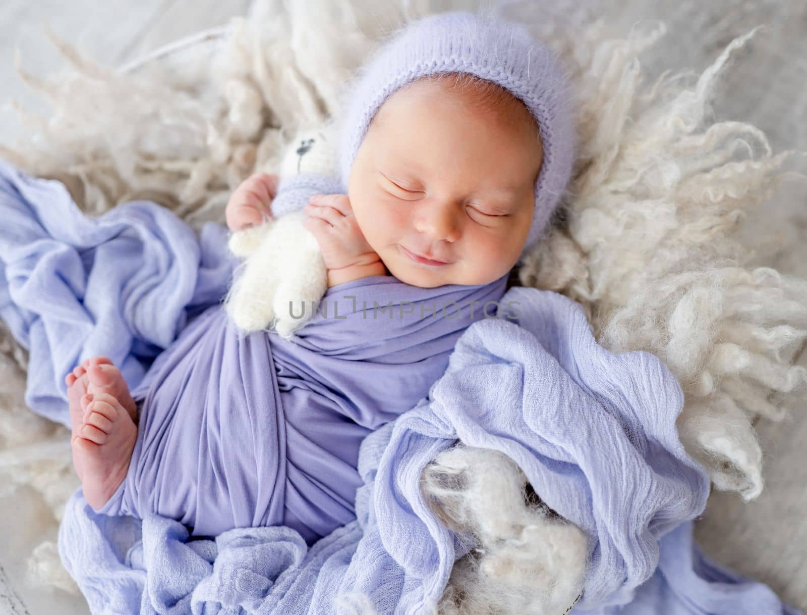 Newborn baby boy sleeping with kitty toy and smiling. Little infant child swaddled in fabric napping