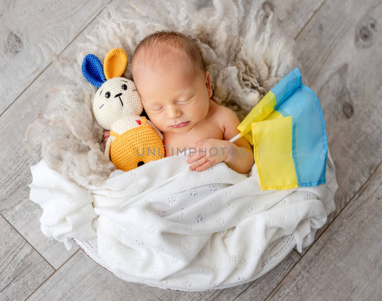 Newborn baby boy sleeping with yellow blue bunny toy and ukrainian flag. Little infant child napping and supporting Ukraine