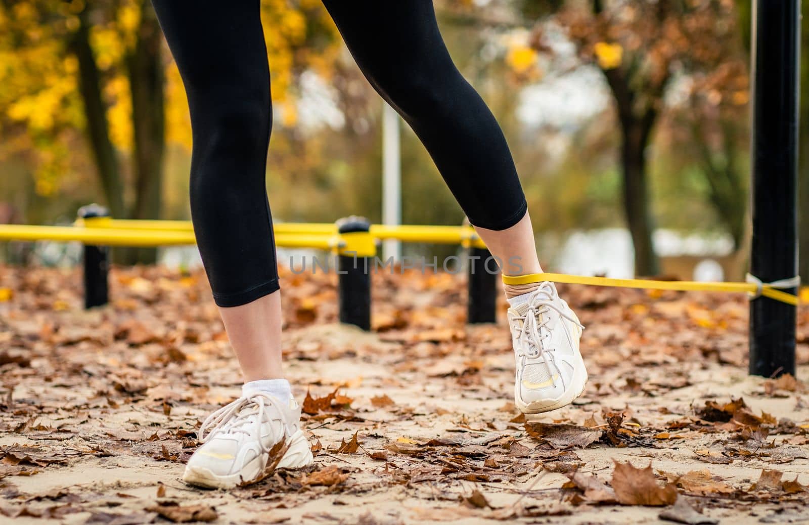 Girl making legs ezxercises with elastic rubber band at autumn time outdoors. Legs training at fall season closeup