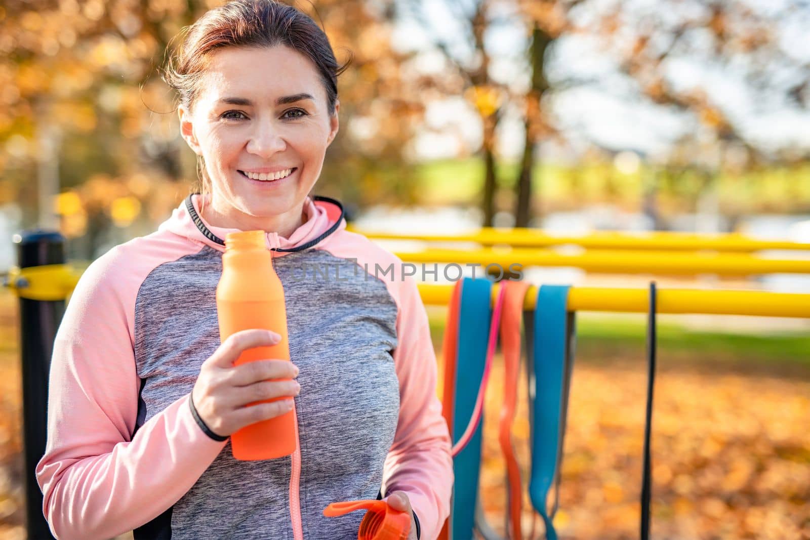 Fitness girl with bottle with water after exercising in autumn park outdoors. Young woman and hydration sport portrait at fall season