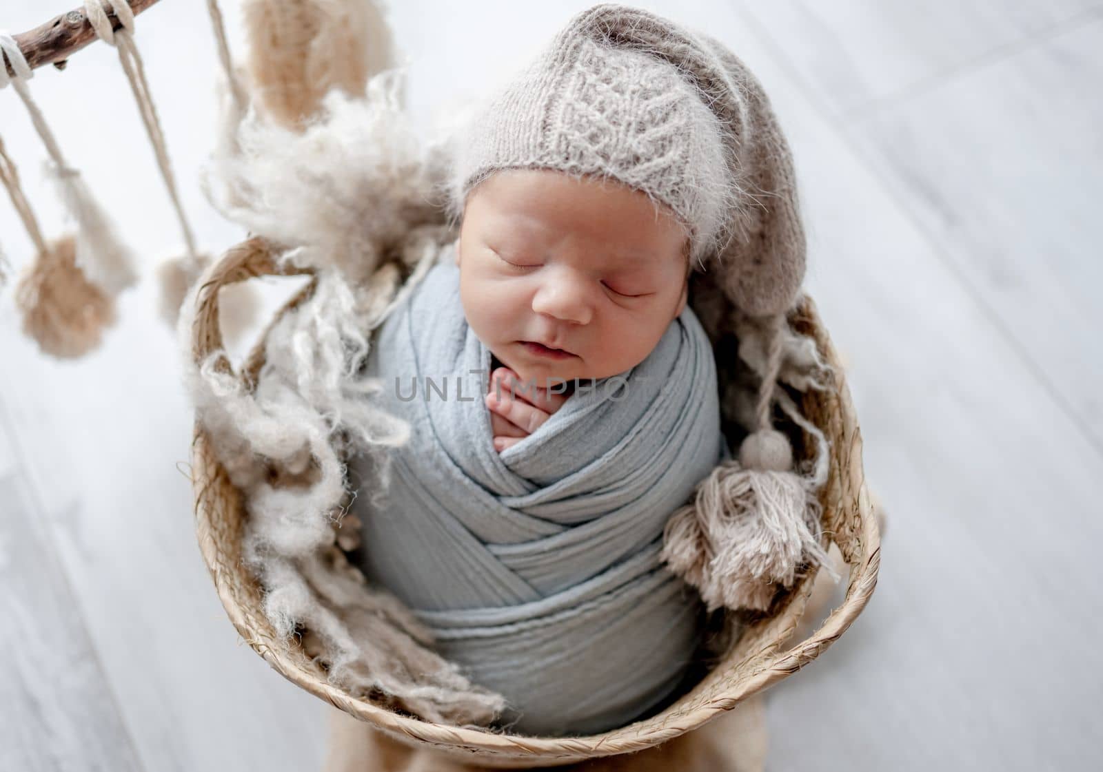 Newborn baby boy swaddled in fabric and wearing hat sleeping in basket studio portrait. Infant child kid napping