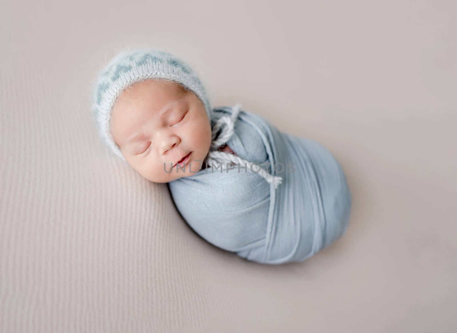 Newborn baby boy sleeping swaddled in fabric studio portrait. Infant child kid napping