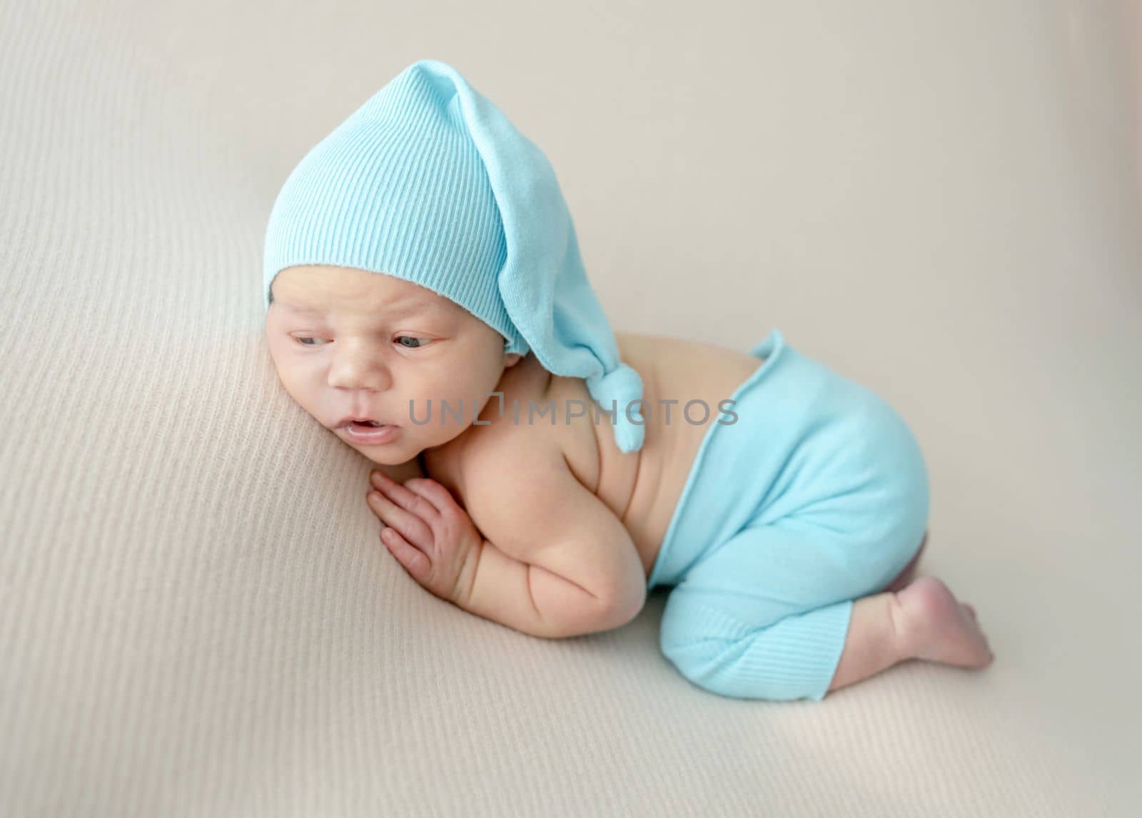 Newborn baby boy wearing knitted pants and hat sleeping on his tummy. Infant child kid napping