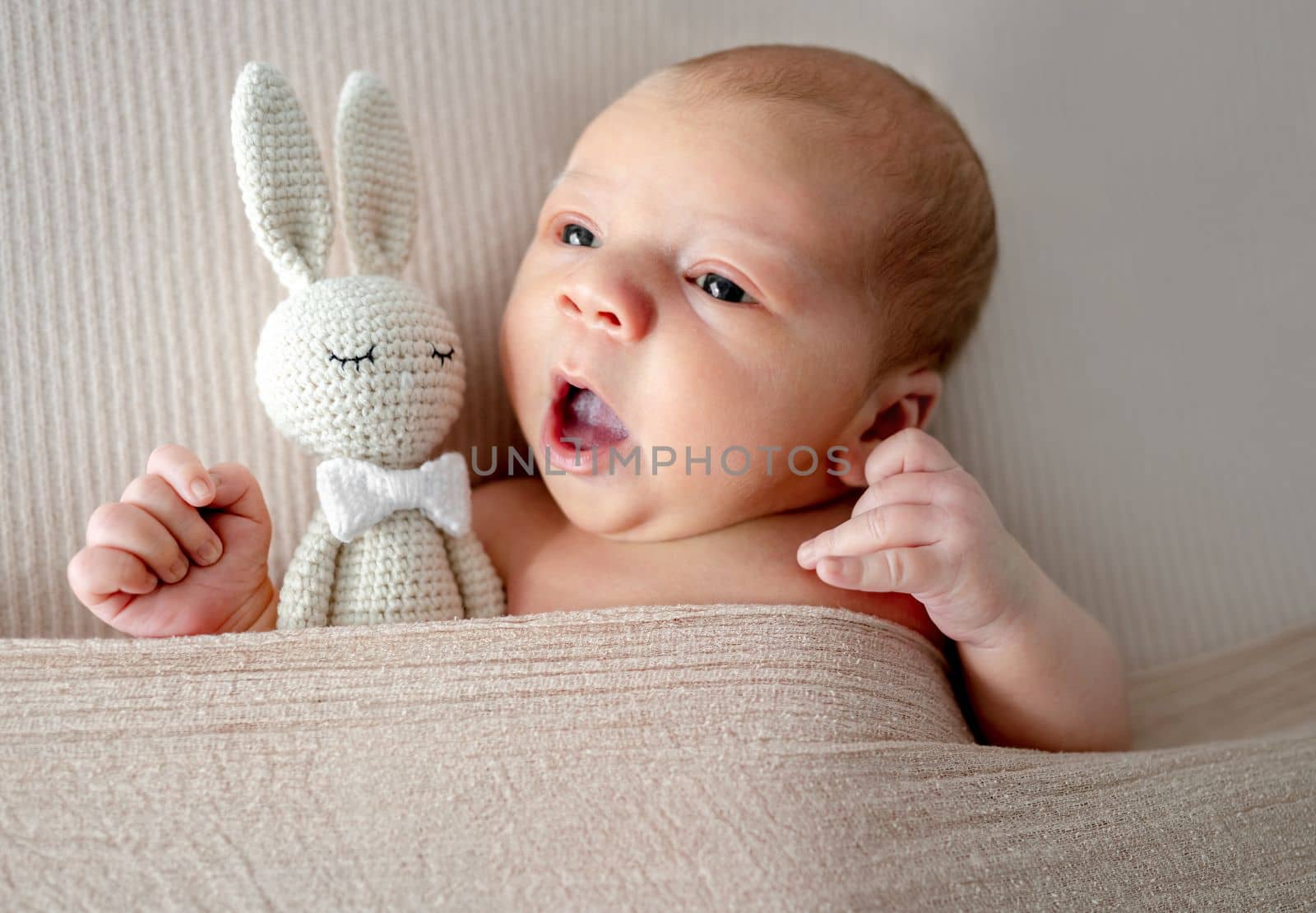 Newborn baby boy yawns and holding knitted bunny toy. Infant child kid napping