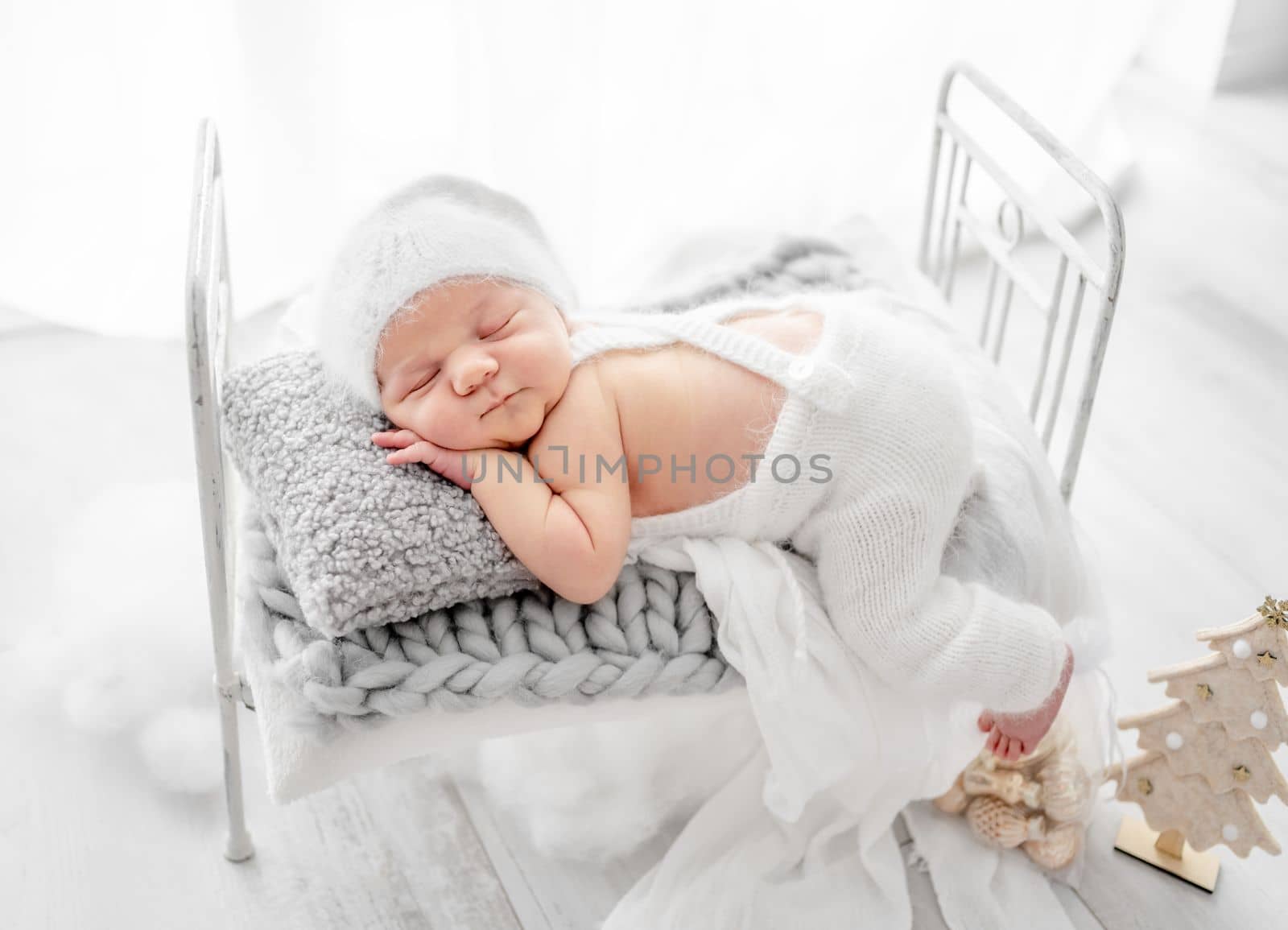 Newborn baby boy wearing knitted pants and hat sleeping on tiny bed studio portrait. Infant child kid napping on his tummy