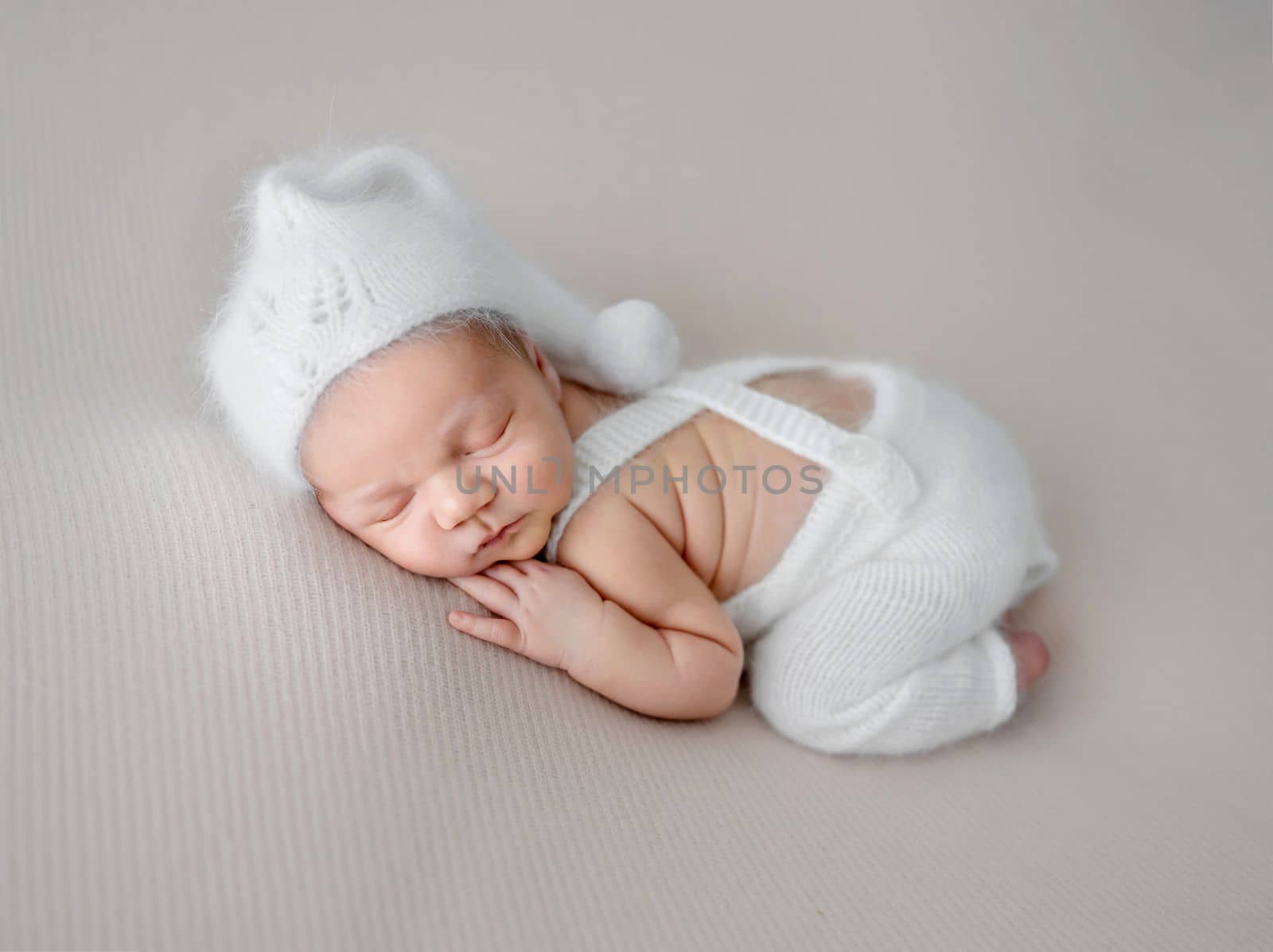 Newborn baby boy wearing knitted pants and hat sleeping on his tummy. Infant child kid napping and holding hand under cheek