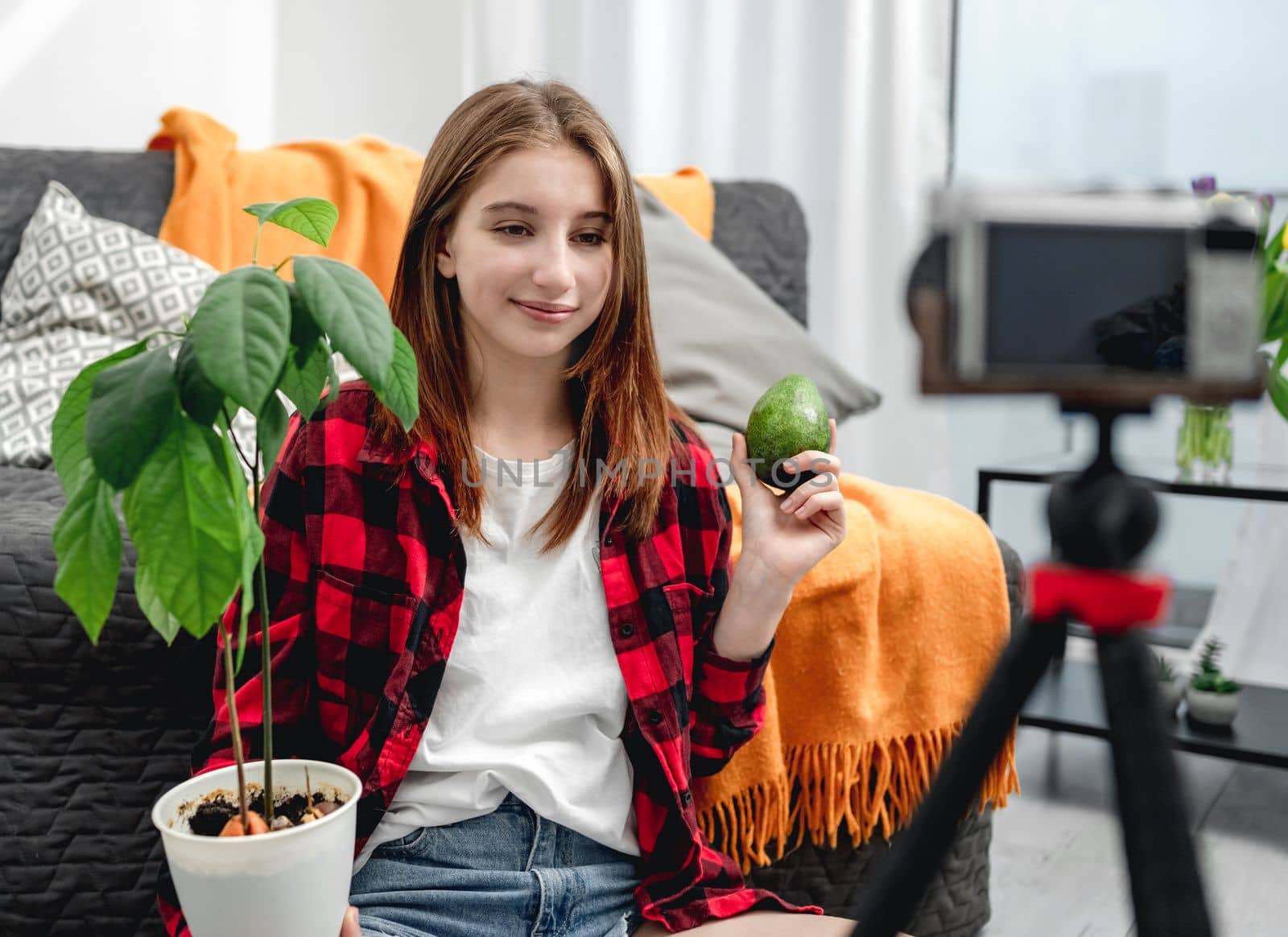 Pretty girl teenager with camera teaching how to grow avocado streaming live video blog for followers in social media. Female blogger filming vlog botanical tutorial