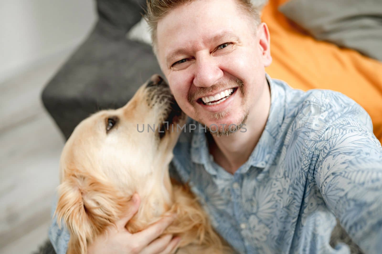 Smiling handsome man with golden retriever dog at home making selfie. Guy with purebred pet doggy labrador indoors