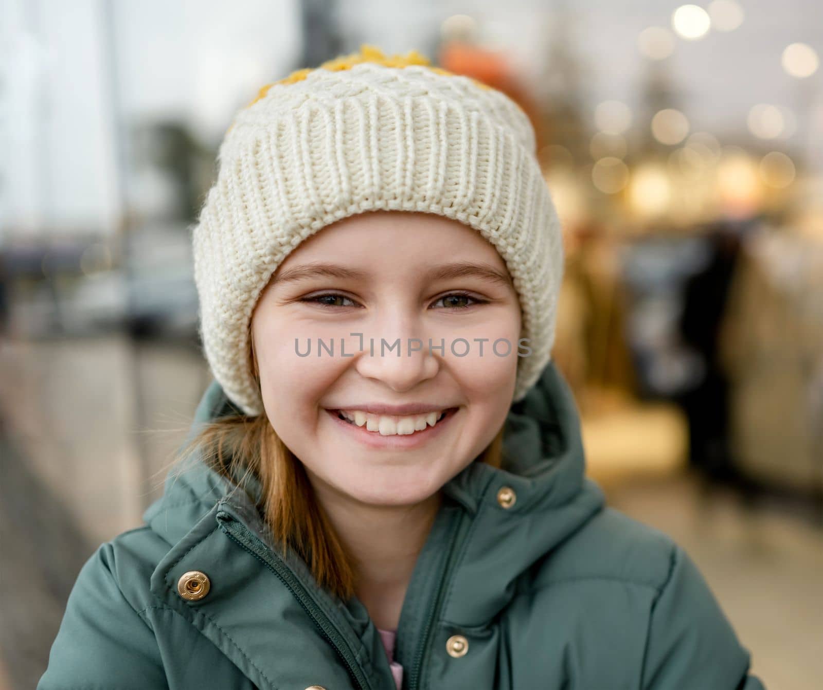 Preteen girl smiling at street portrait in city with blurred background. Cute female child kid wearing hat outdoors at autumn time