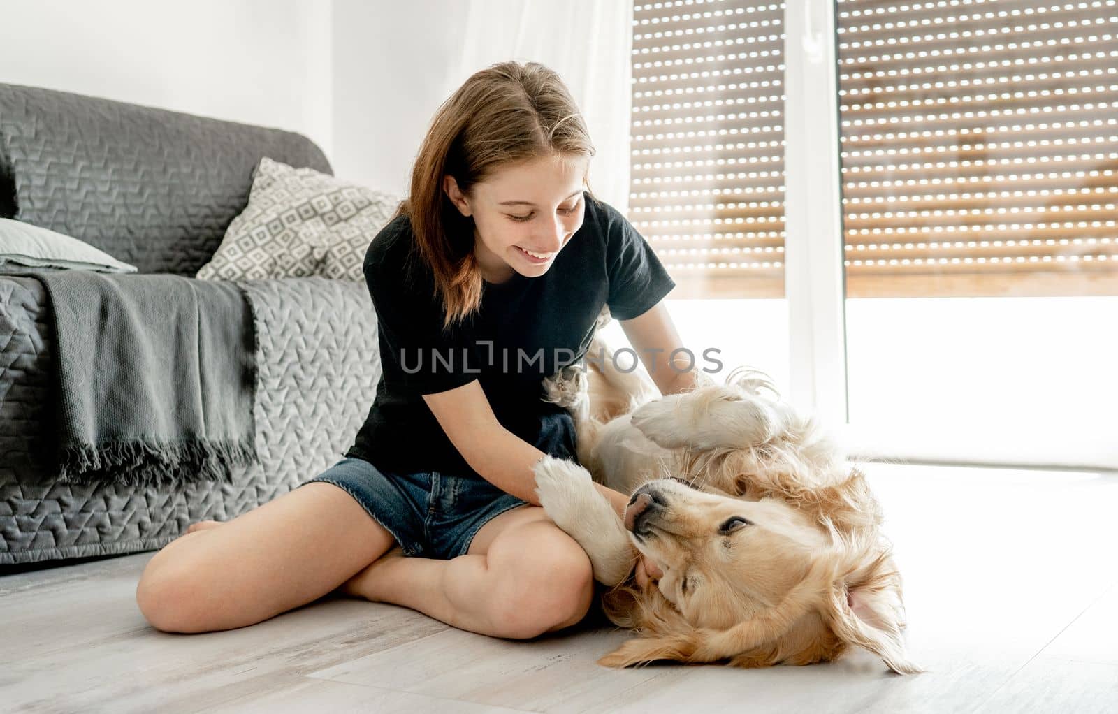 Pretty girl with golden retriever dog sitting on floor at home and petting pet friend. Beautiful female teenager person with purebred doggy