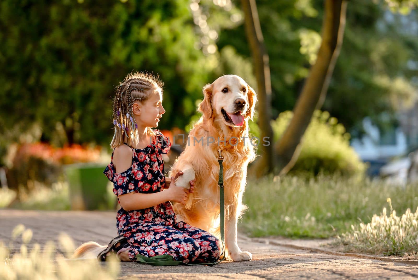 Preteen girl with golden retriever dog sitting in park in beautiful summer day. Adorable female child kid hugging purebred doggy pet outdoors portrait