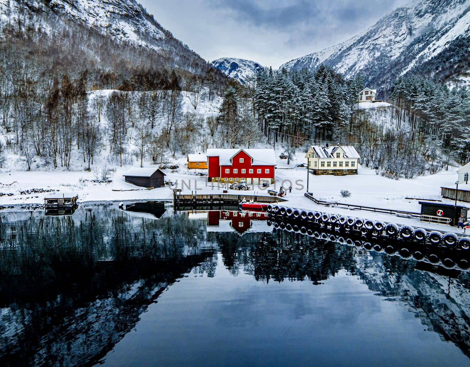 Charming village in Norway with wooden red houses surrounded with snowy mountains and lake with reflection in winter. Scenery scandinavian landscape with sea view in Europe
