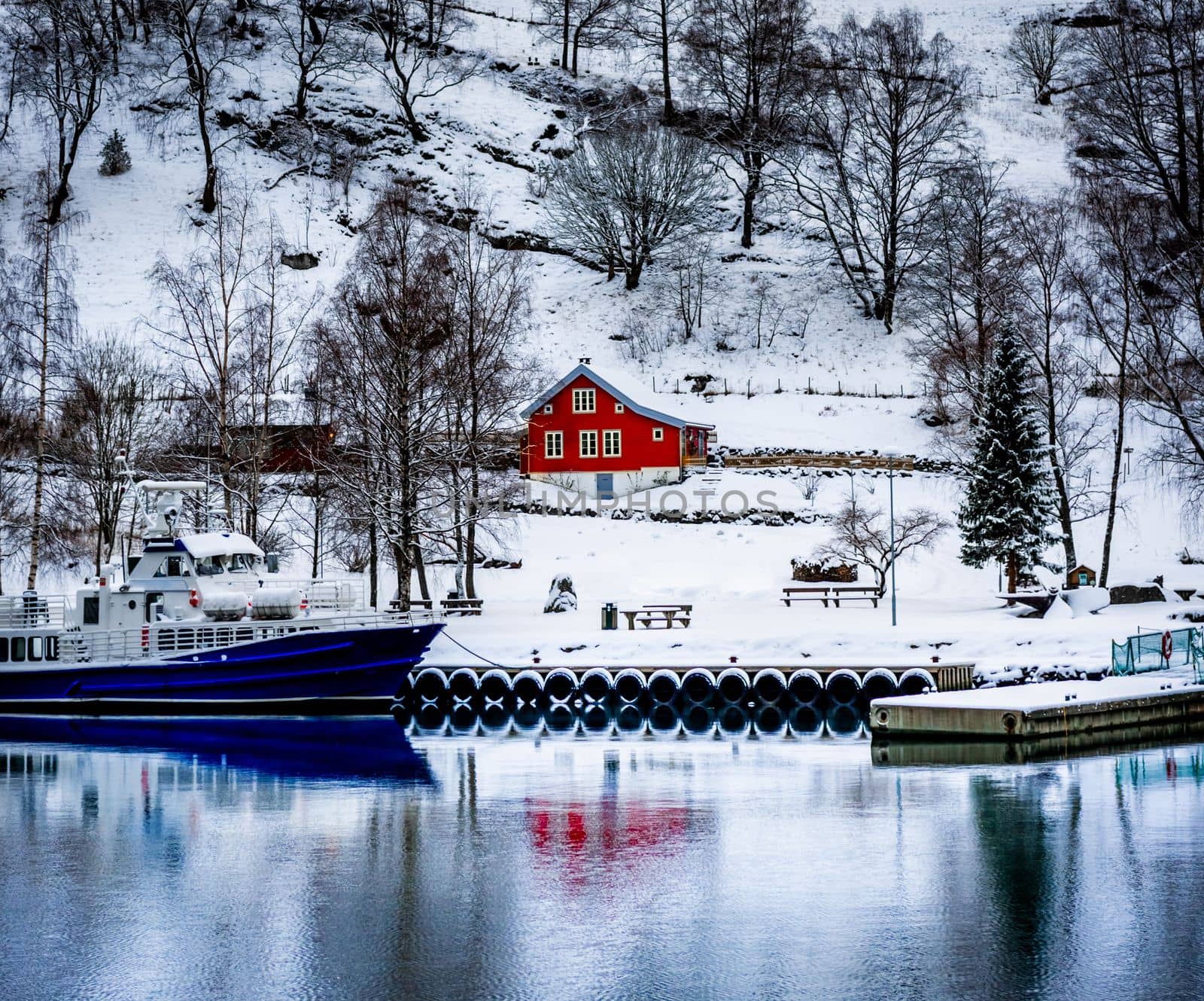 Charming village in Norway with wooden red house and boat with reflection in cold lake in winter. Scenery scandinavian landscape with sea view in Europe