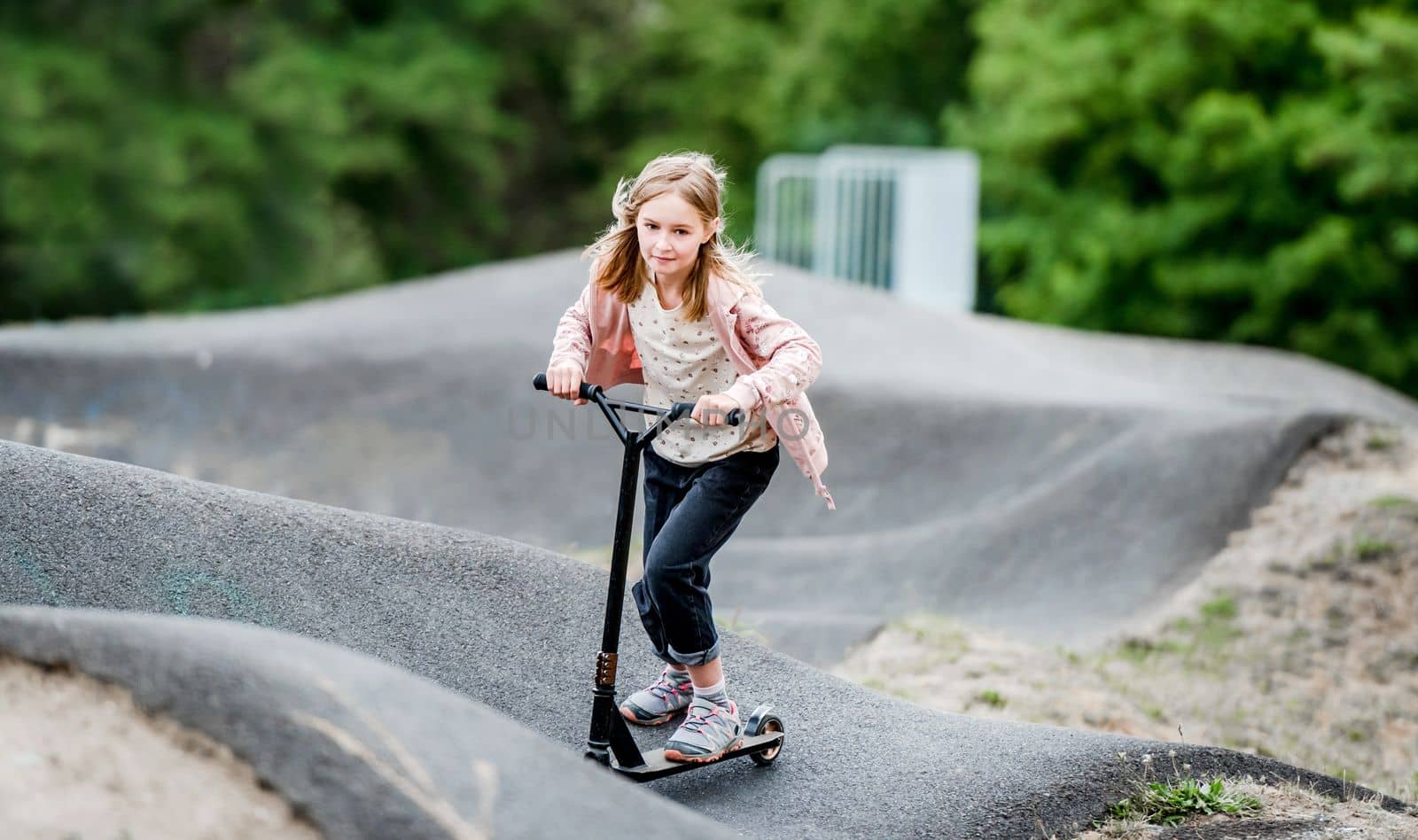 Preteen girl riding scooter in city park at spring time. Pretty child kid having fun with vehicle outdoors