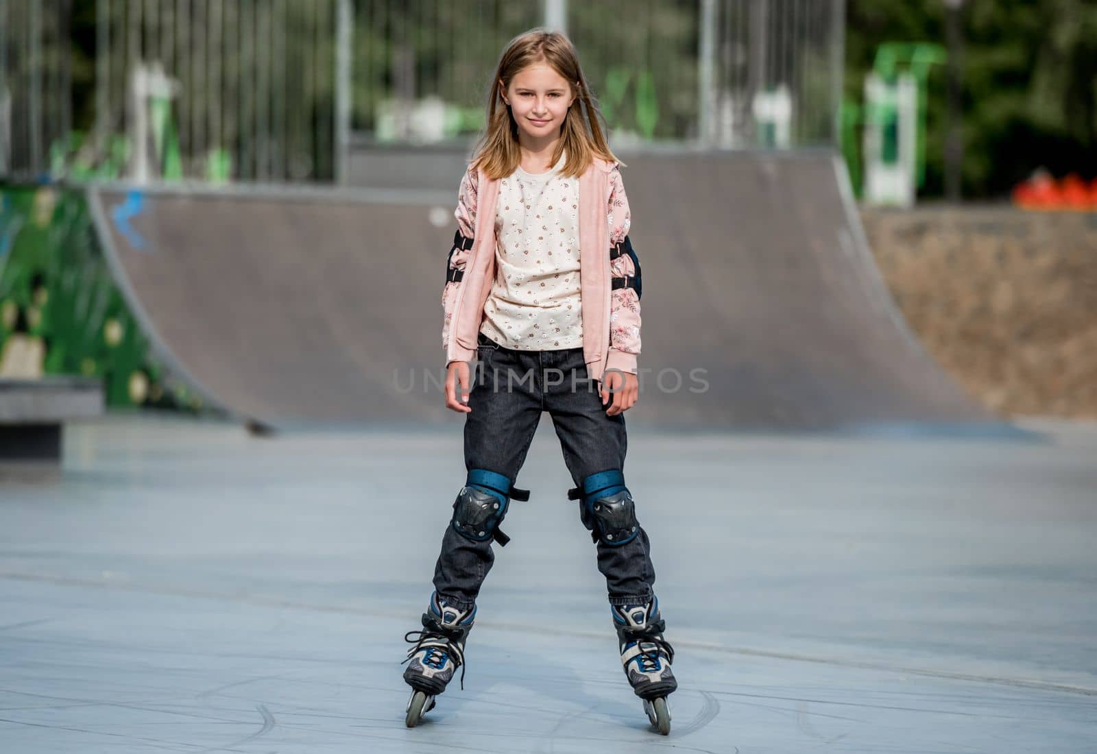 Cute girl roller skater riding in city park. Pretty female preteen child kid rollerskating with sunlight outdoors