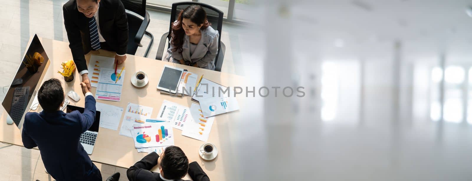 Group business people handshake at meeting table in widen view in office together with confident shot from top view . Young businessman and businesswoman workers express agreement of investment deal.