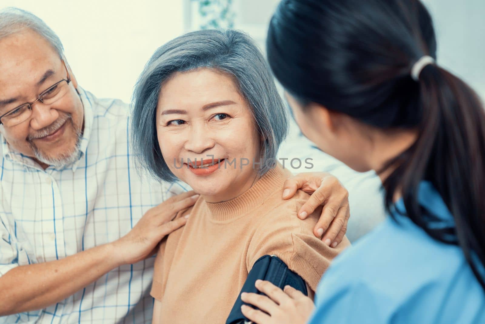 An elderly woman with a contented life having a blood pressure check by her caregiver at home with a smiley face.