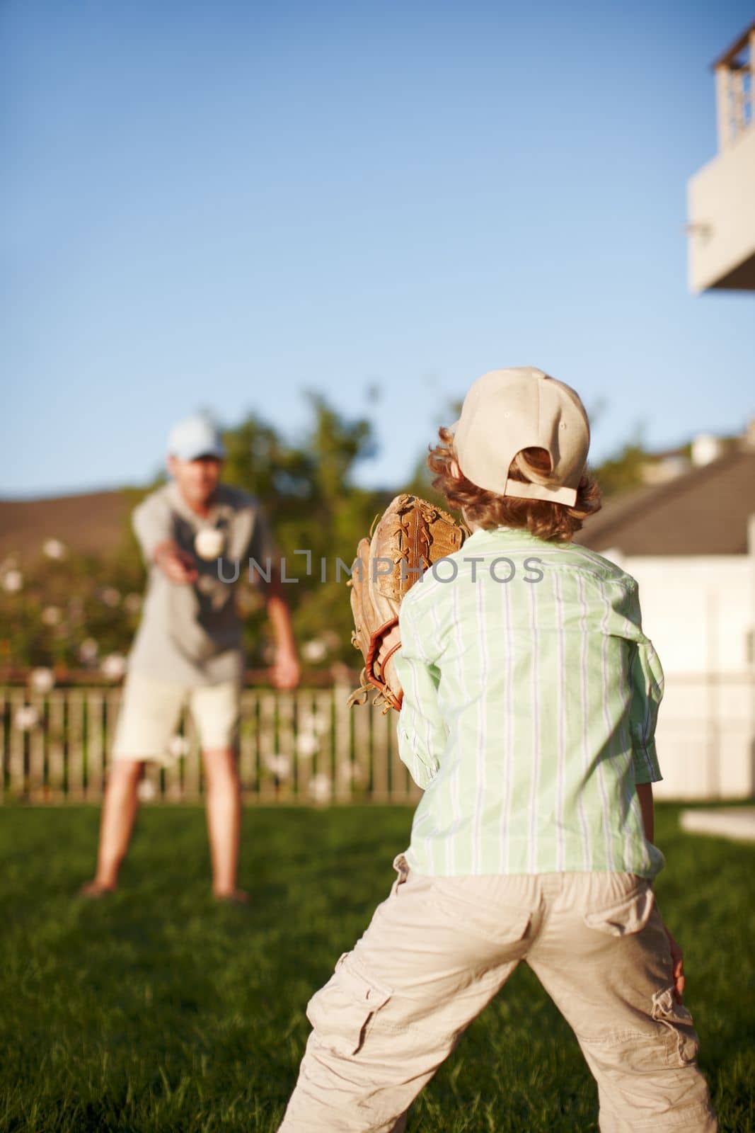 Playing catch. a father and son throwing the baseball outdoors in the yard. by YuriArcurs