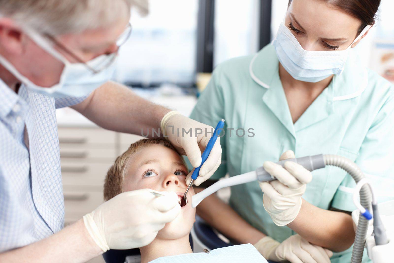 Visit at the dentists surgery. Portrait of dentist operating young boys teeth in clinic. by YuriArcurs