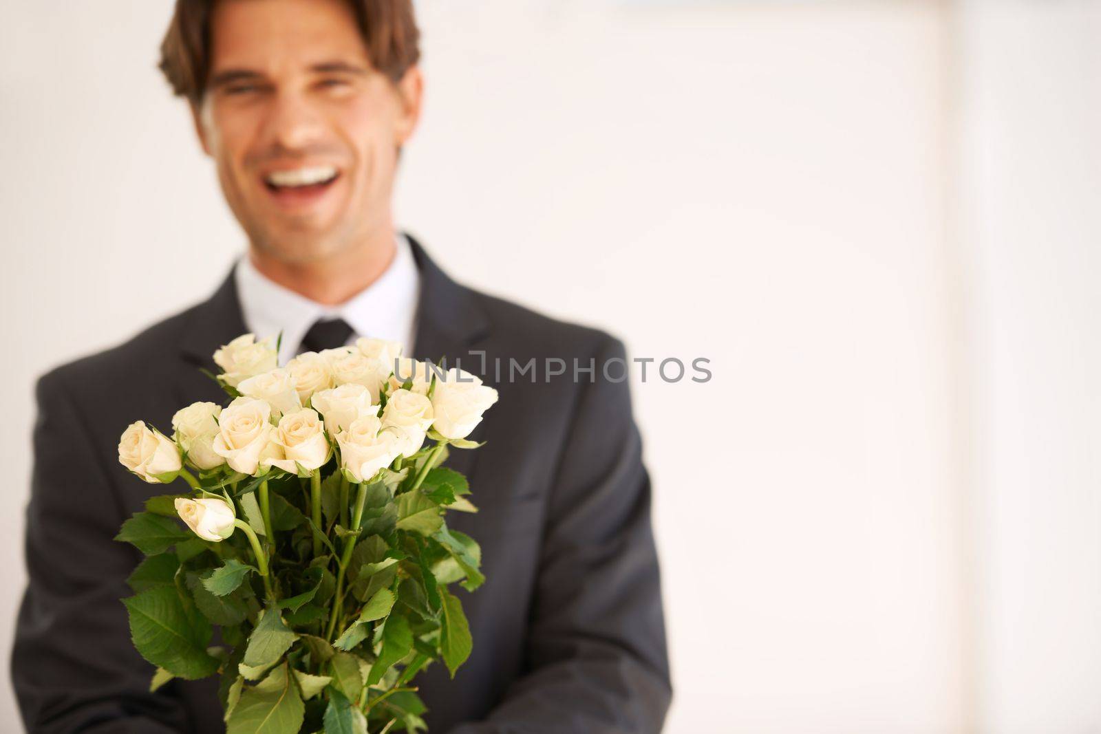 He is the romantic type. Portrait of a handsome young man wearing a suit and holding a bunch of roses. by YuriArcurs