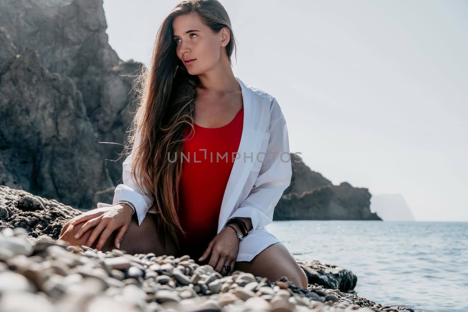 Young woman in red bikini on Beach. Girl lying on pebble beach and enjoying sun. Happy lady with long hair in bathing suit chilling and sunbathing by turquoise sea ocean on hot summer day. Close up by panophotograph