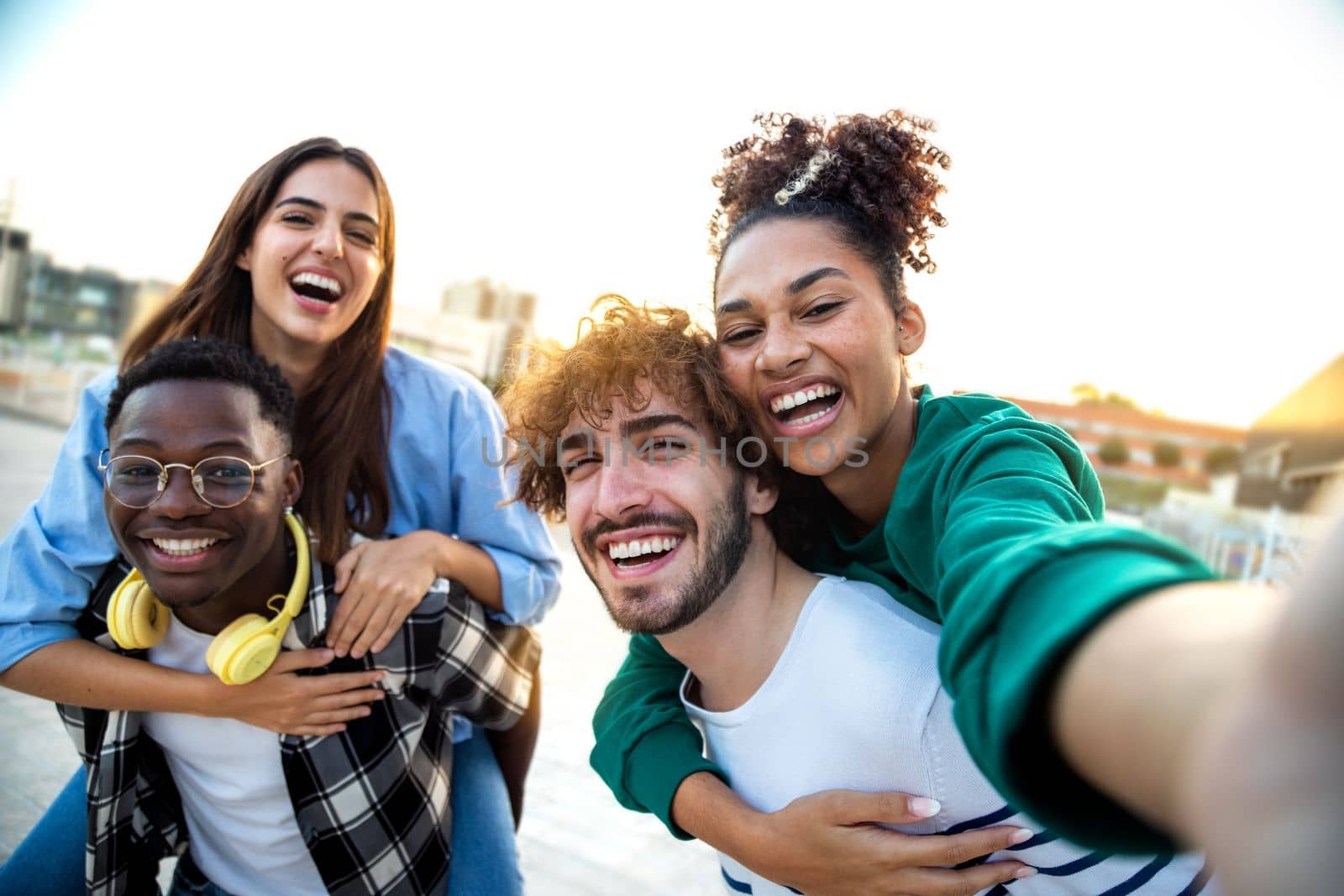 Multiracial happy friends having fun taking group selfie portrait on city street. Young multicultural people celebrating laughing together outdoors. Happy lifestyle concept.