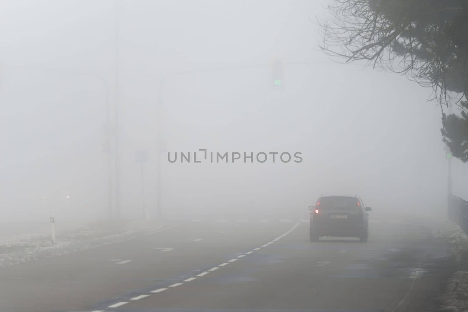 Car traveling on the foggy road with headlights or headlamps on. Low visibility - Dangerous driving of cars in winter in bad weather.