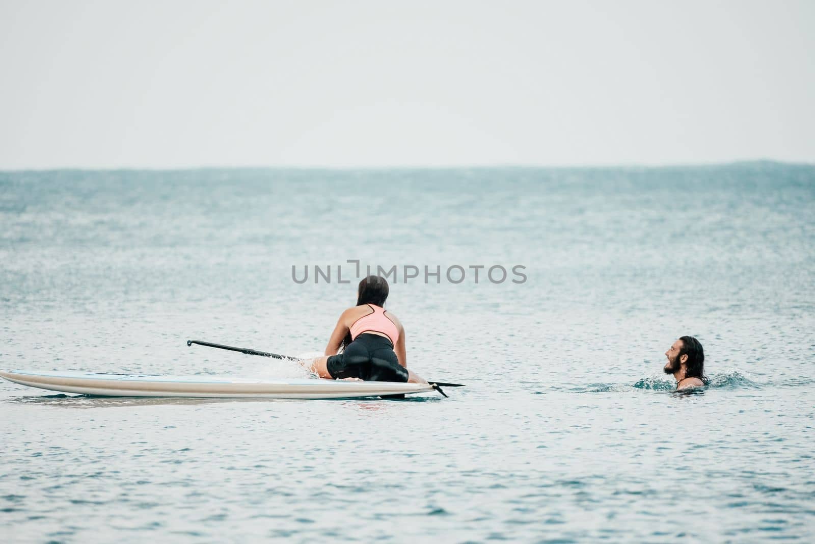 Sea woman and man on sup. Silhouette of happy young woman and man, surfing on SUP board, confident paddling through water surface. Idyllic sunset. Active lifestyle at sea or river