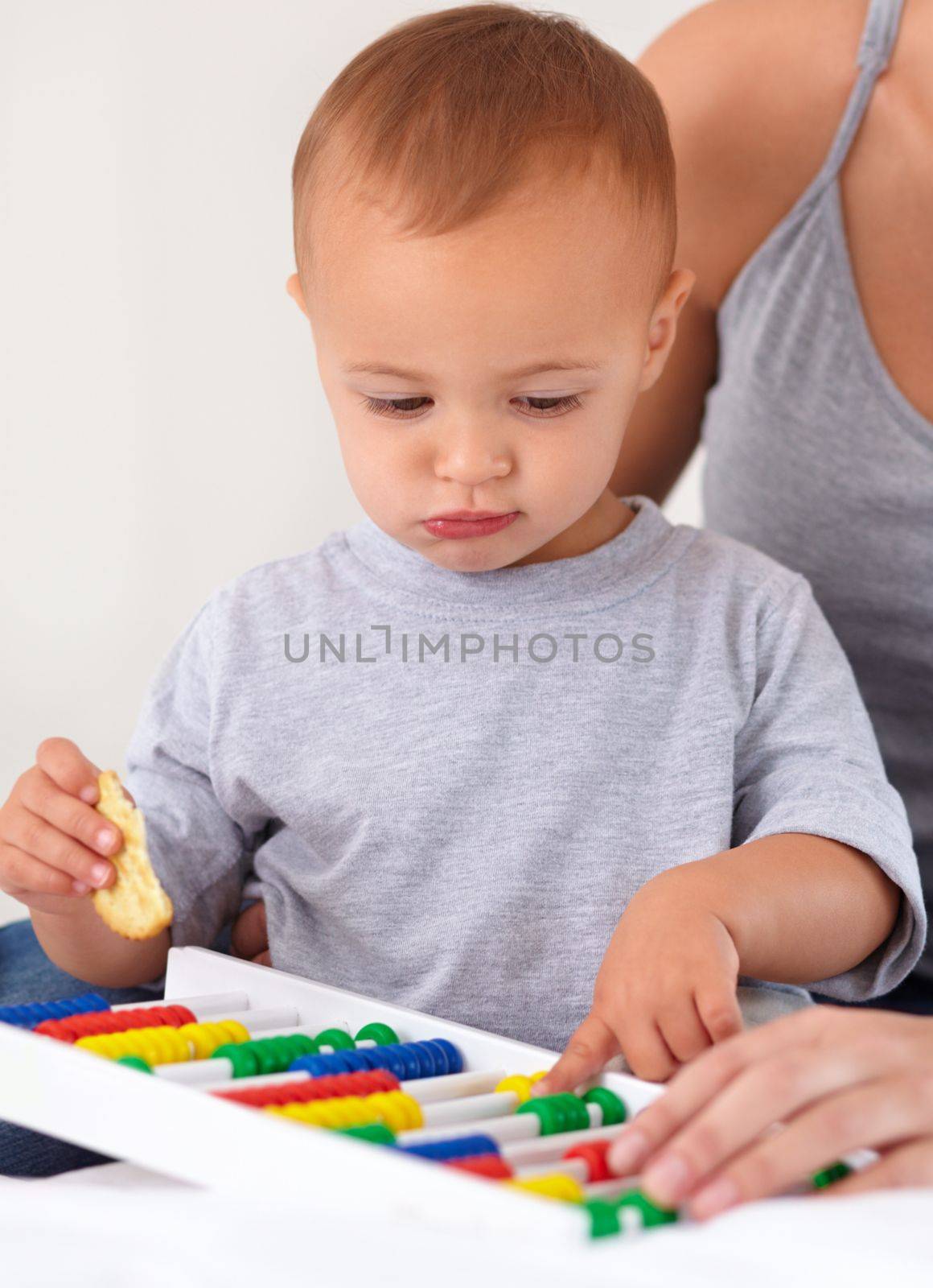 Learning with mommys help. A toddler boy playing with an abacus and eating a cracker