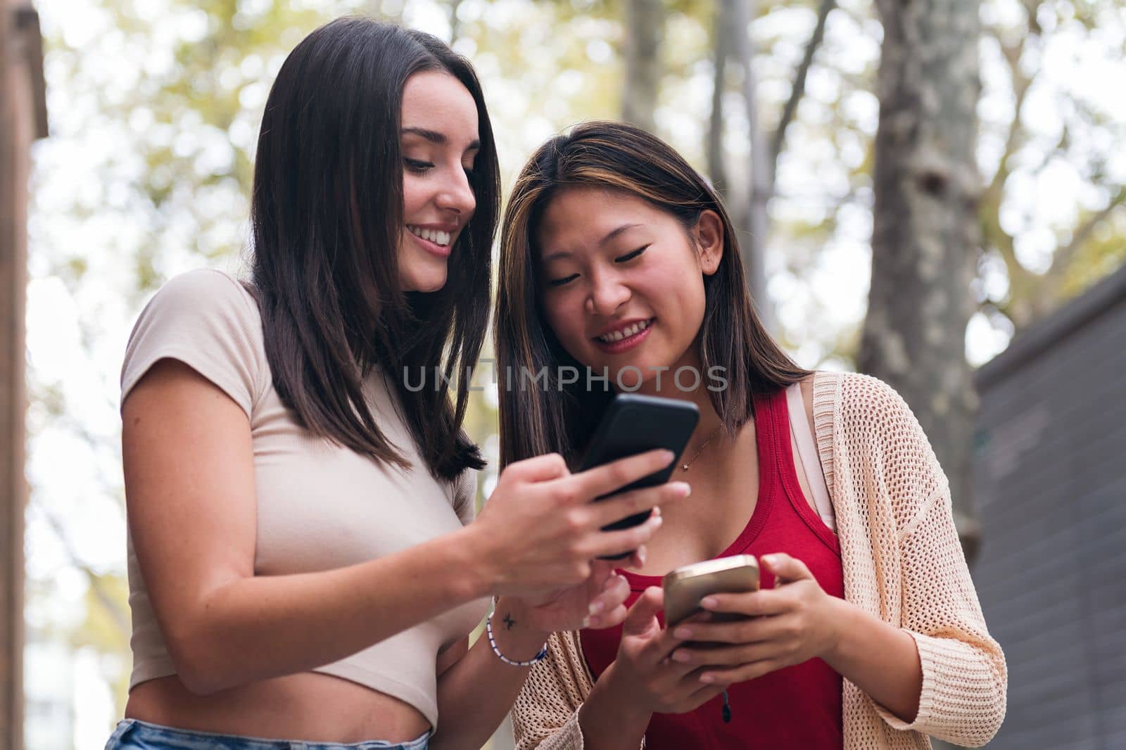 two young women sharing confidences and having fun with their cell phones, concept of friendship and technology of communication
