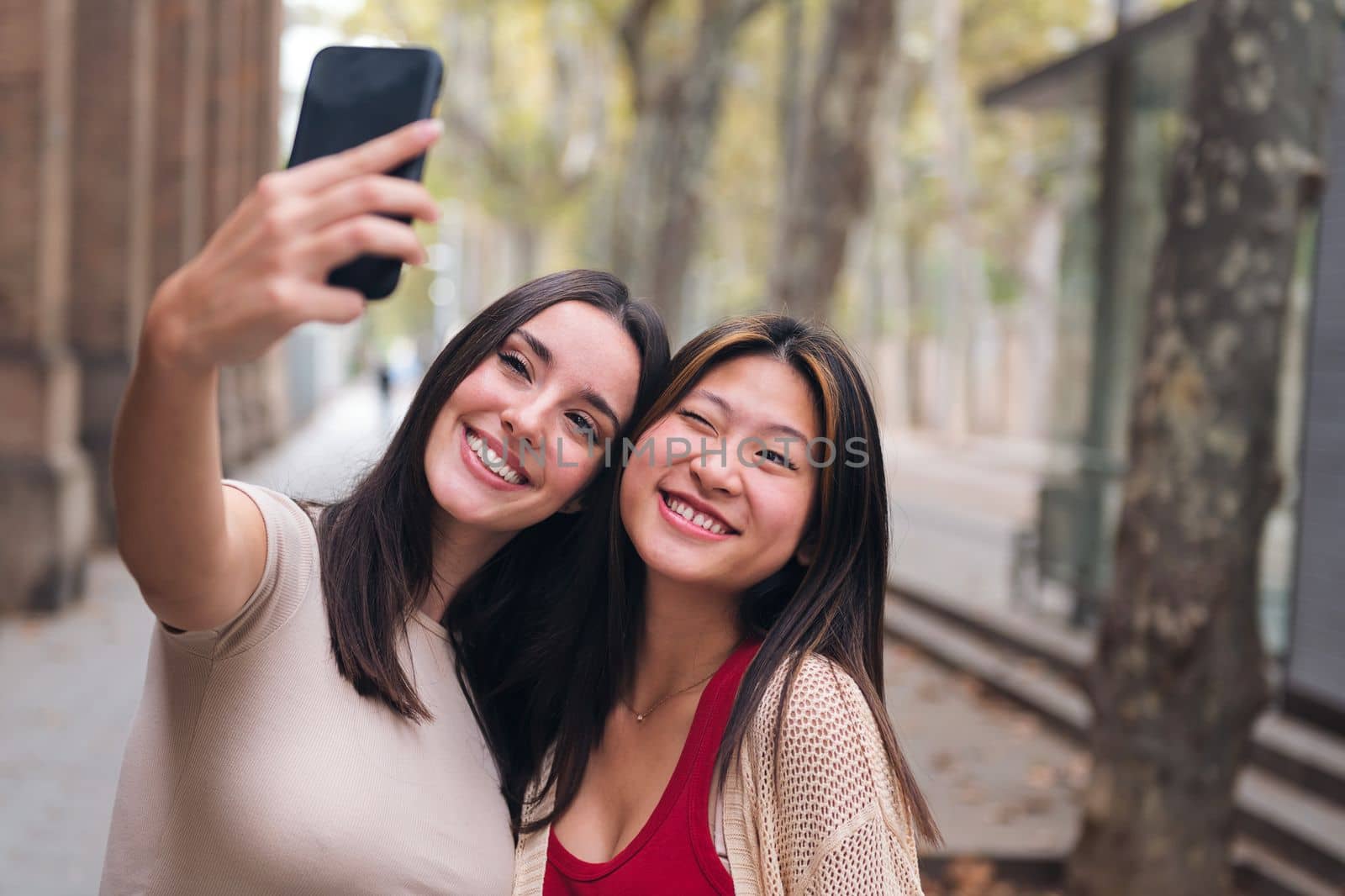 two young women smiling and having fun taking a selfie photo with a cell phone, concept of friendship and technology of communication