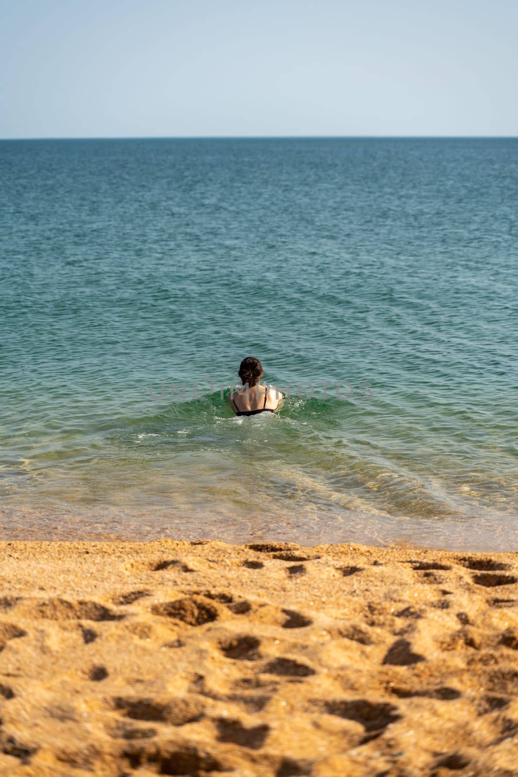 Woman sea swimsuit sand. The girl swims in the sea in a black swimsuit, the water is clean and transparent. Alone on the beach on a sunny day. by Matiunina