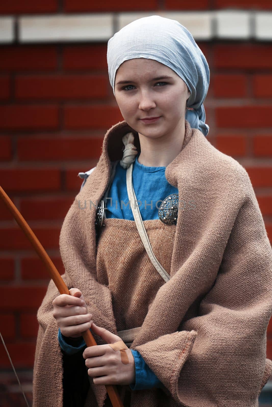 Portrait of a young girl in a medieval castle with a wooden bow in her hands. A little girl in medieval dress walking through a yard. historical reconstruction. 14.05,2022. Yoshkar-Ola, Russia.