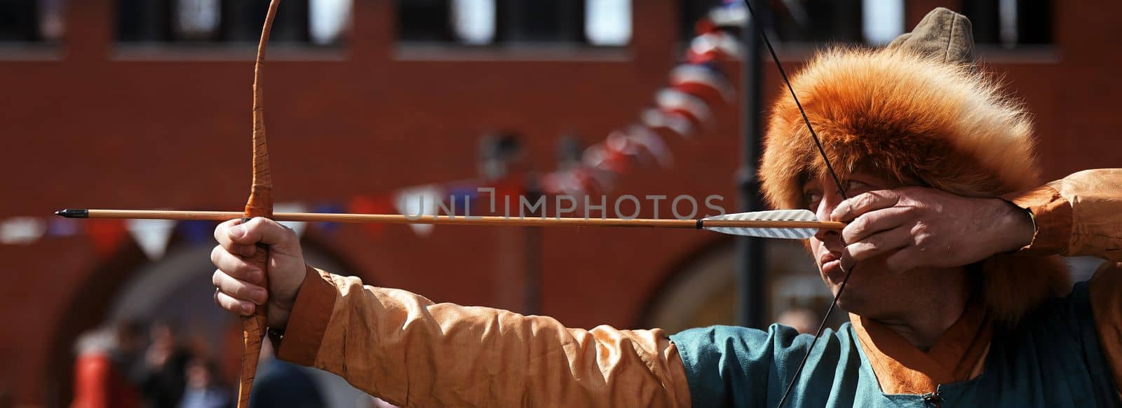 Medieval archery tournament. Man shoots an arrow in the medieval castle yard. Man in medieval dress with a wooden bow in her hands. historical reconstruction. 14.05,2022. Yoshkar-Ola, Russia by EvgeniyQW